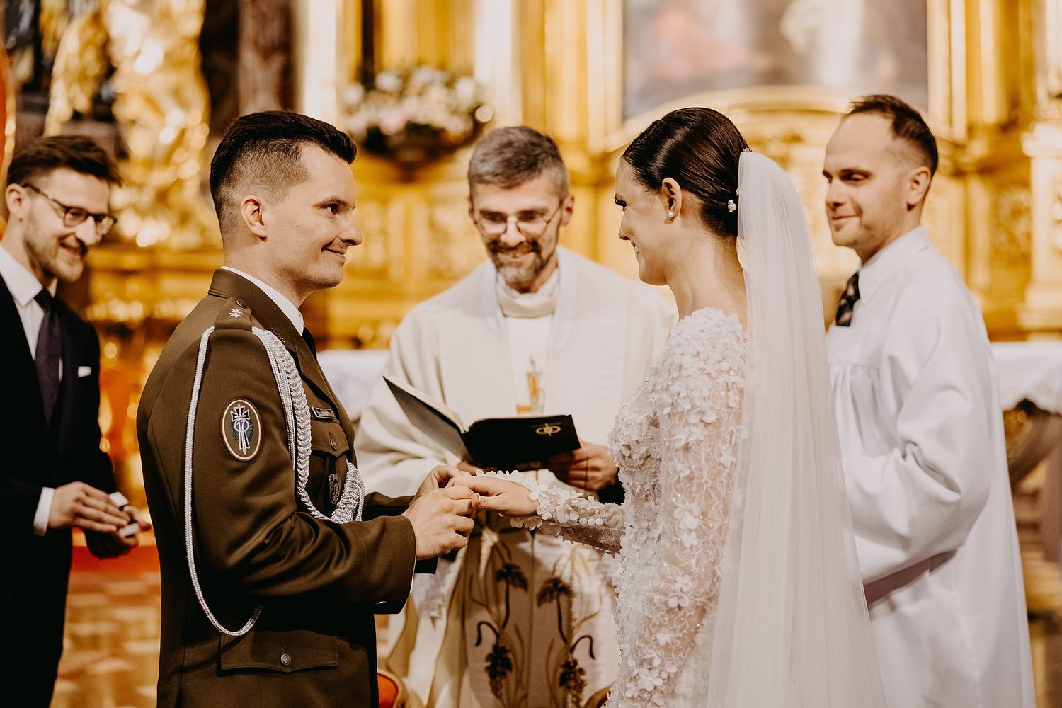 Groom in military uniform exchanging rings with bride at church altar with smiling officiant.