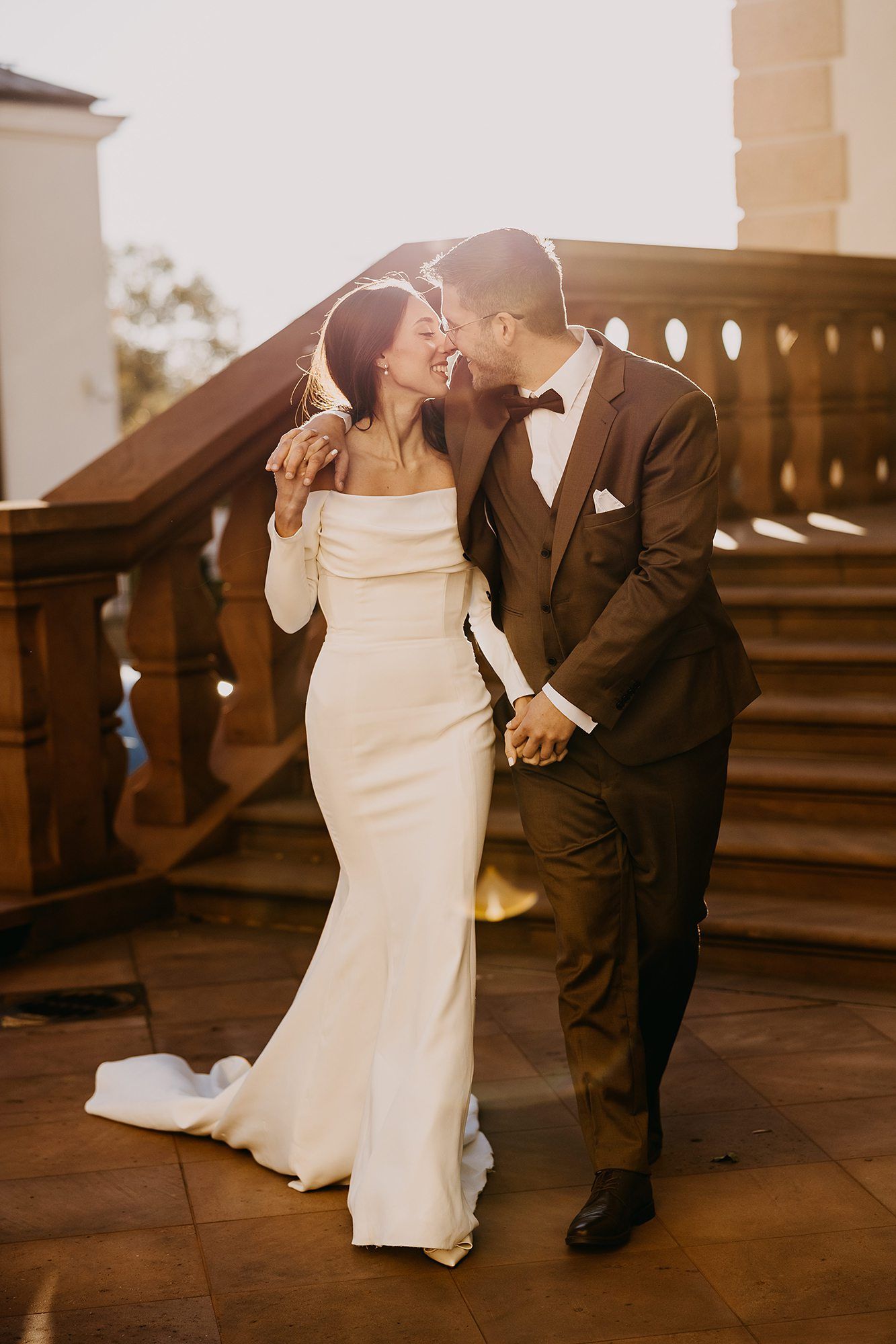Bride and groom sharing a tender kiss on sunlit stone staircase.