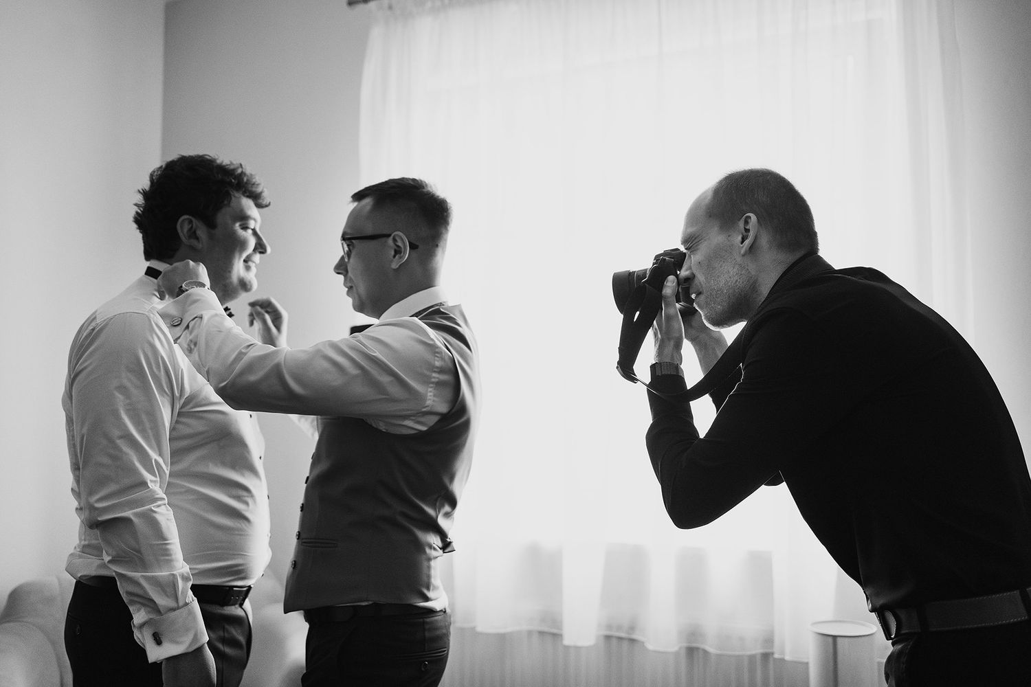 Black and white photo of photographer capturing man adjusting another mans collar.