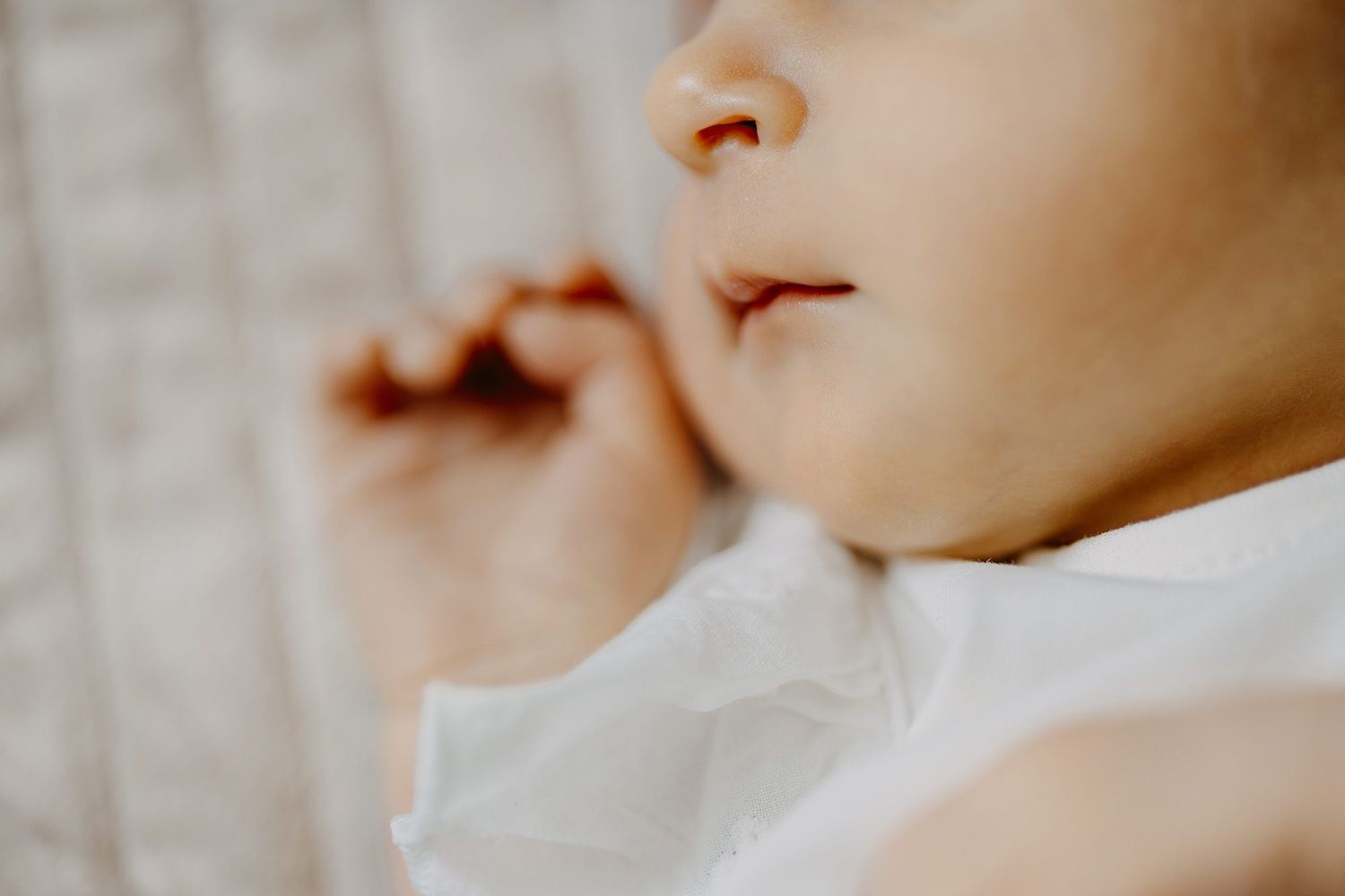 Close-up of sleeping newborn baby in white crib with tiny fist raised.