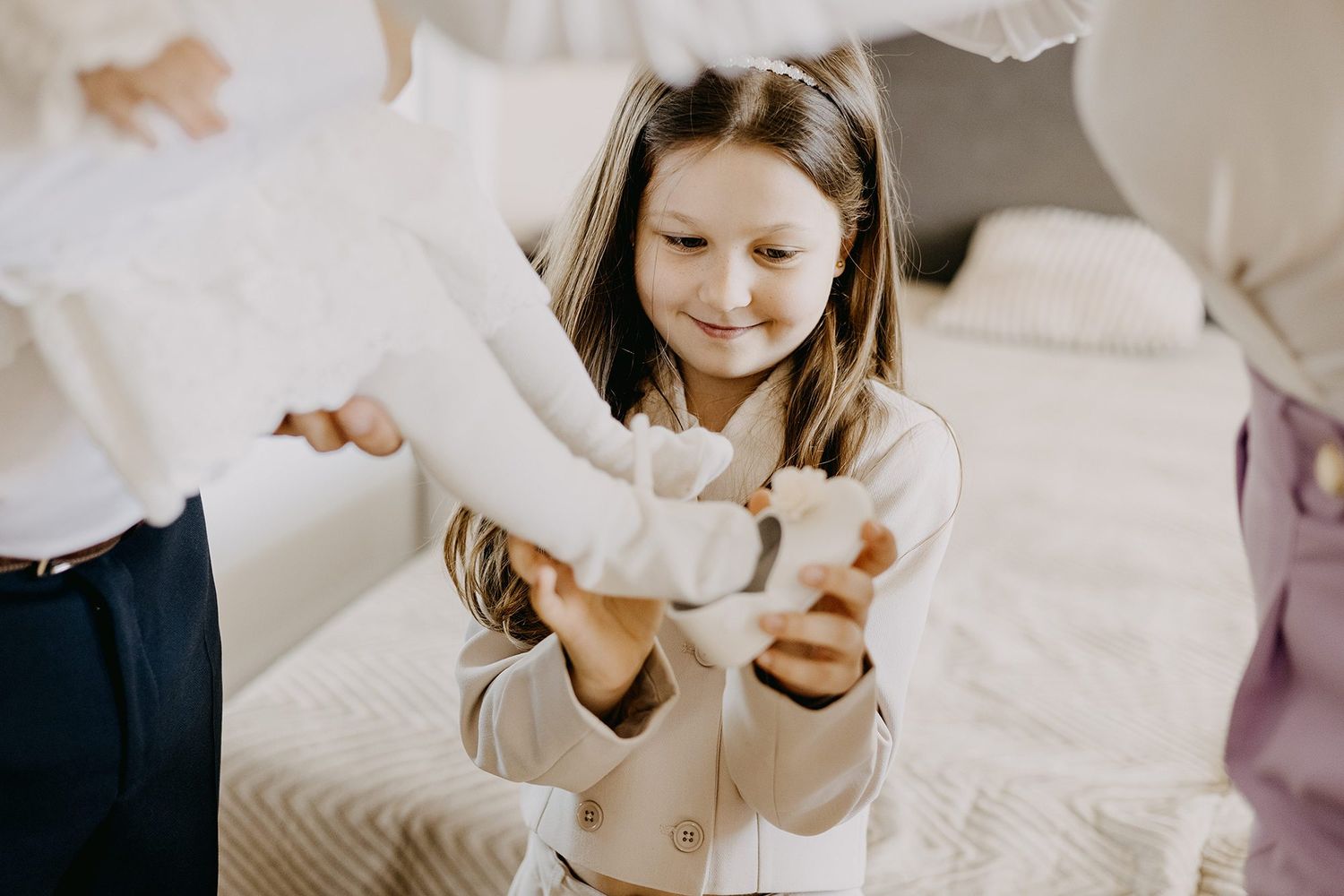 A young girl in a cream outfit smiles while holding a white stuffed animal toy.