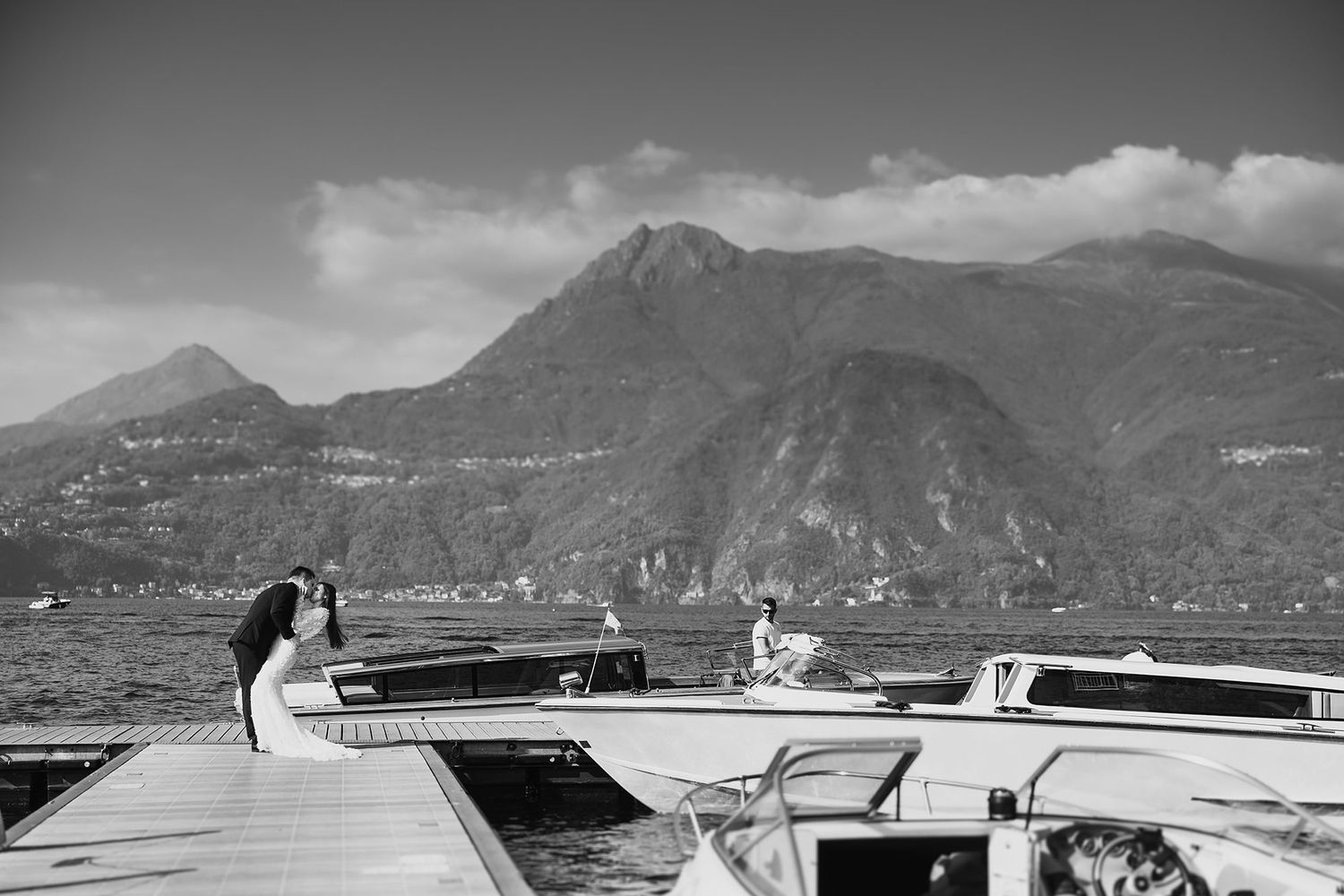 Black and white photo of wedding couple on a boat dock with dramatic mountain backdrop.