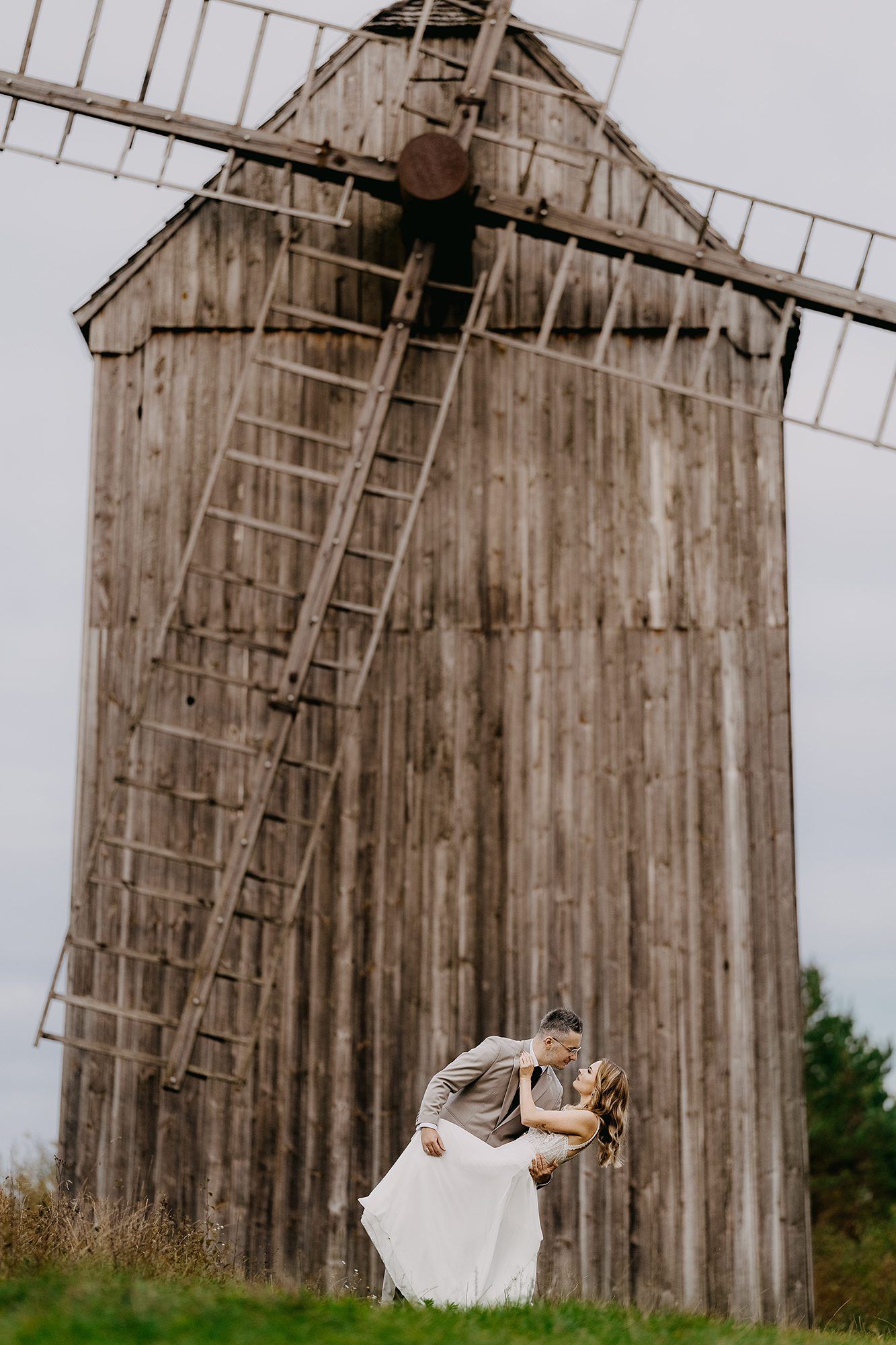 Wedding couple sharing a romantic dip kiss in front of a rustic wooden windmill on their wedding day.