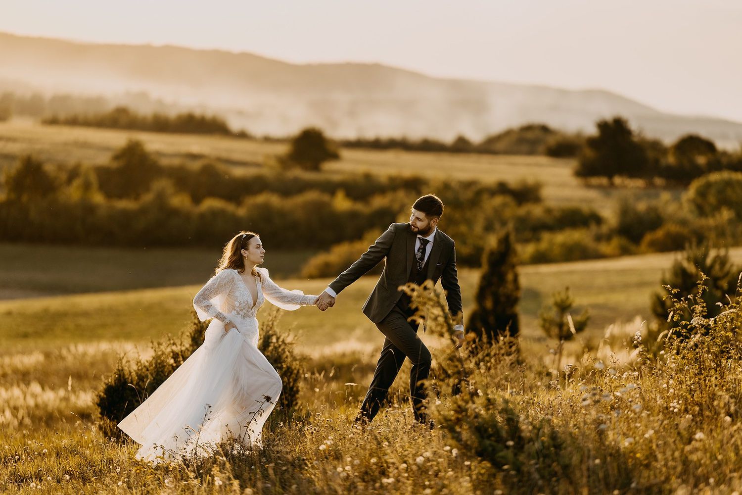 Bride and groom running hand in hand through a beautiful golden meadow during sunset.