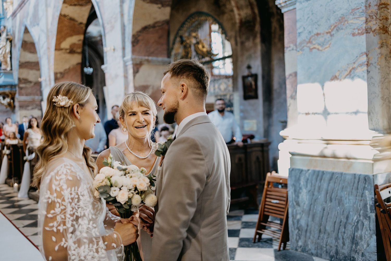 Bride and groom sharing a joyful moment with a smiling guest during a church wedding ceremony.