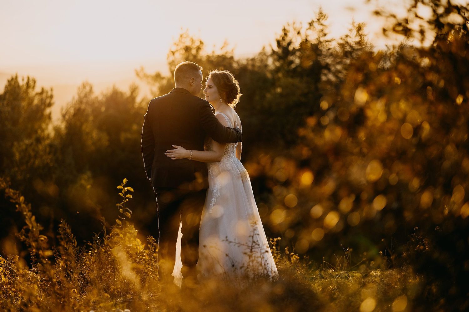 Bride and groom sharing romantic moment in golden sunset light outdoors.