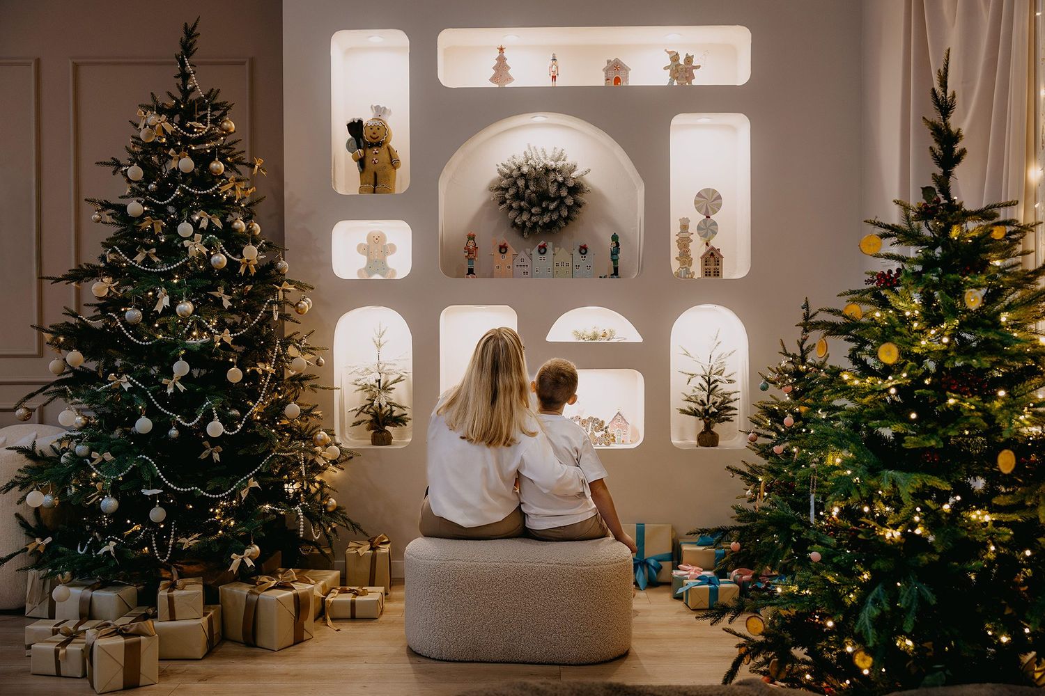 A mother and child sit together viewing a beautifully decorated room with two Christmas trees and wrapped gifts.