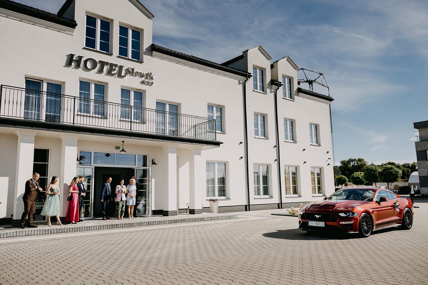Wedding guests gathered outside Hotel Plaza with a red Ford Mustang Shelby parked in front.