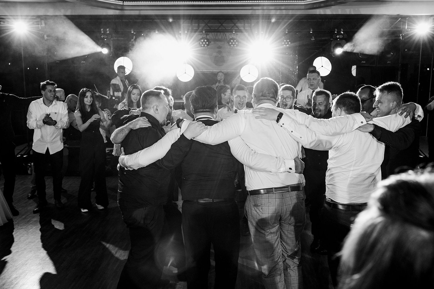 Black and white photo of wedding guests forming a circle on the dance floor during reception.
