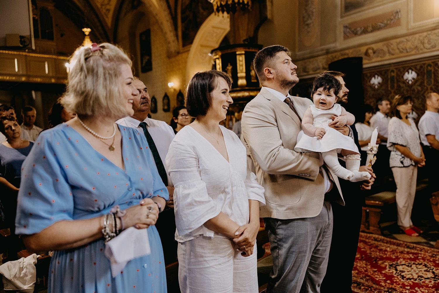 Family group with baby in arms smiling together inside ornate church interior.