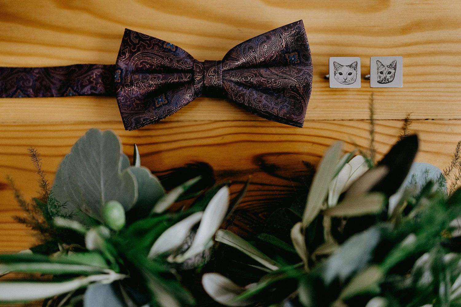 Purple paisley bow tie with cat cufflinks and green floral bouquet.