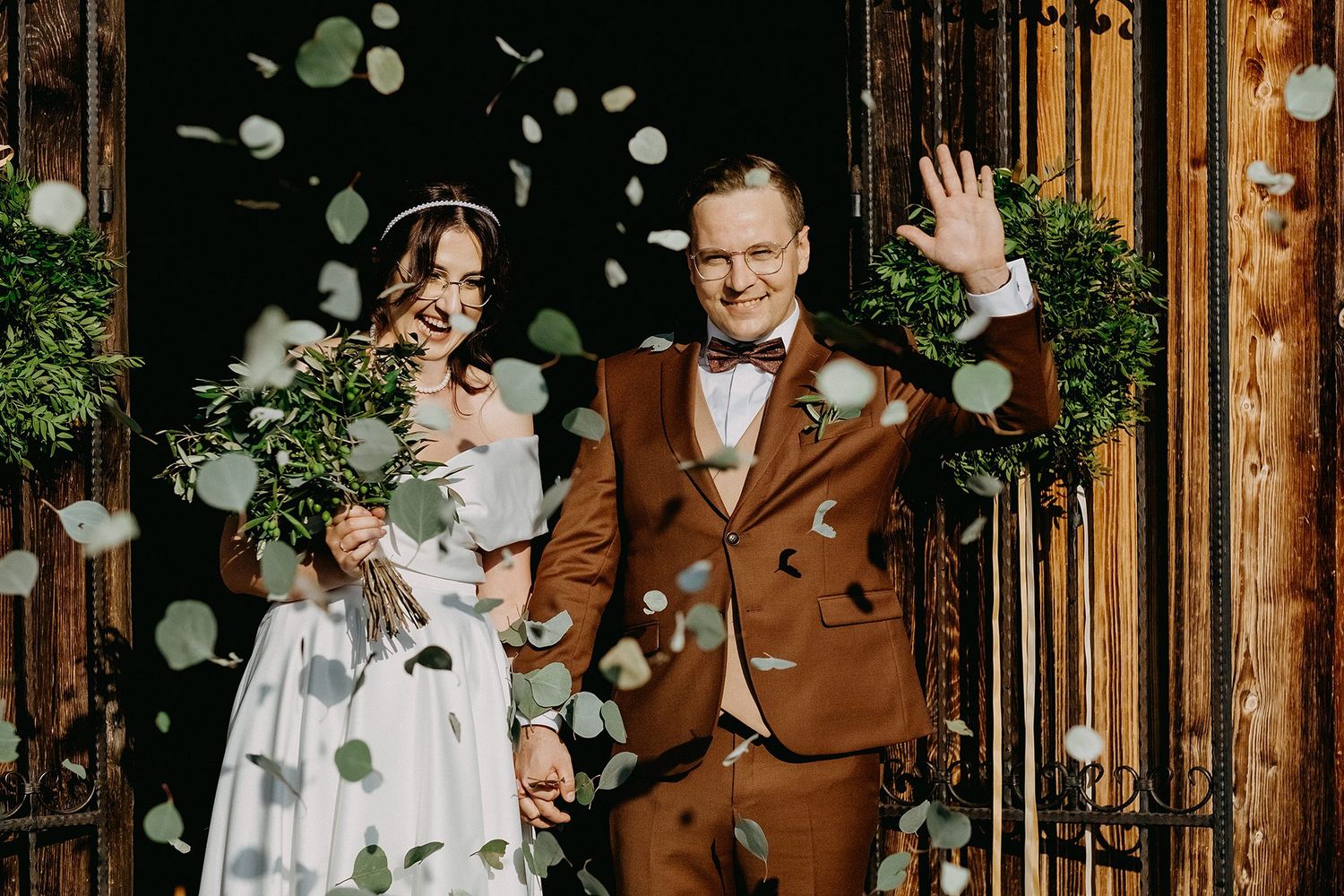 Newlyweds exit church doors as guests toss green leaf confetti in joyful celebration.