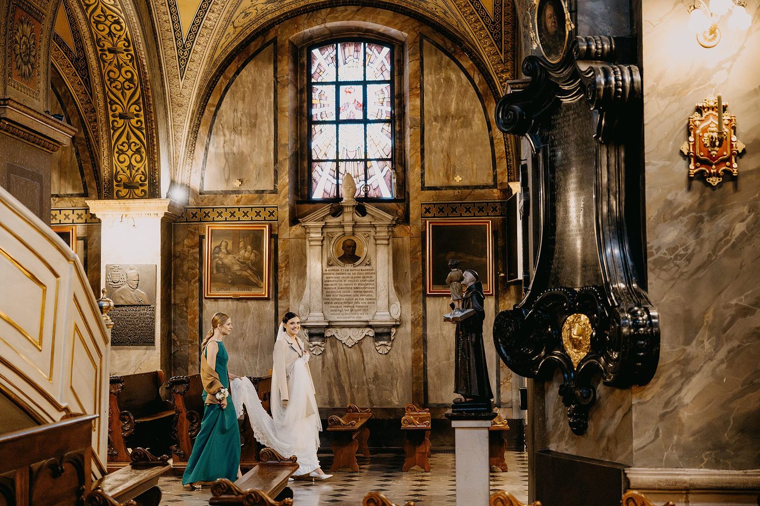 Bride and groom walking through an ornate historic church interior with golden decor and stained glass windows.
