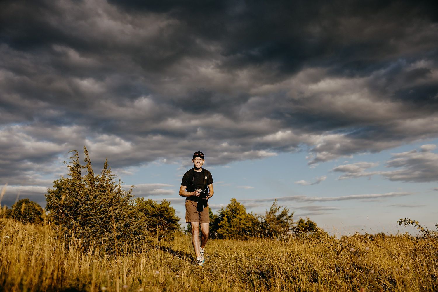 Man running through golden grass field under dramatic cloudy sky at sunset.