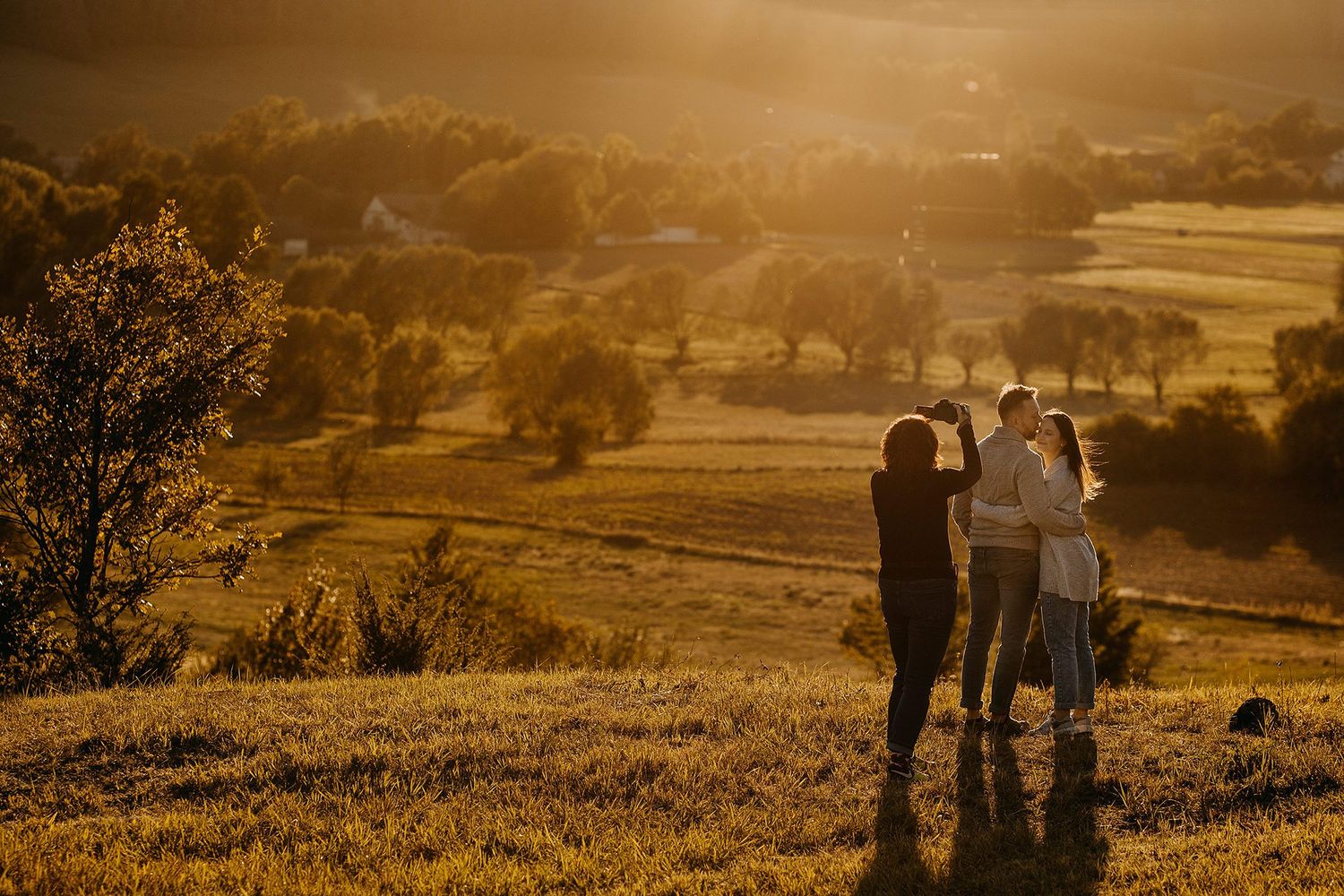 Three people photographing stunning golden sunset over rural valley landscape.