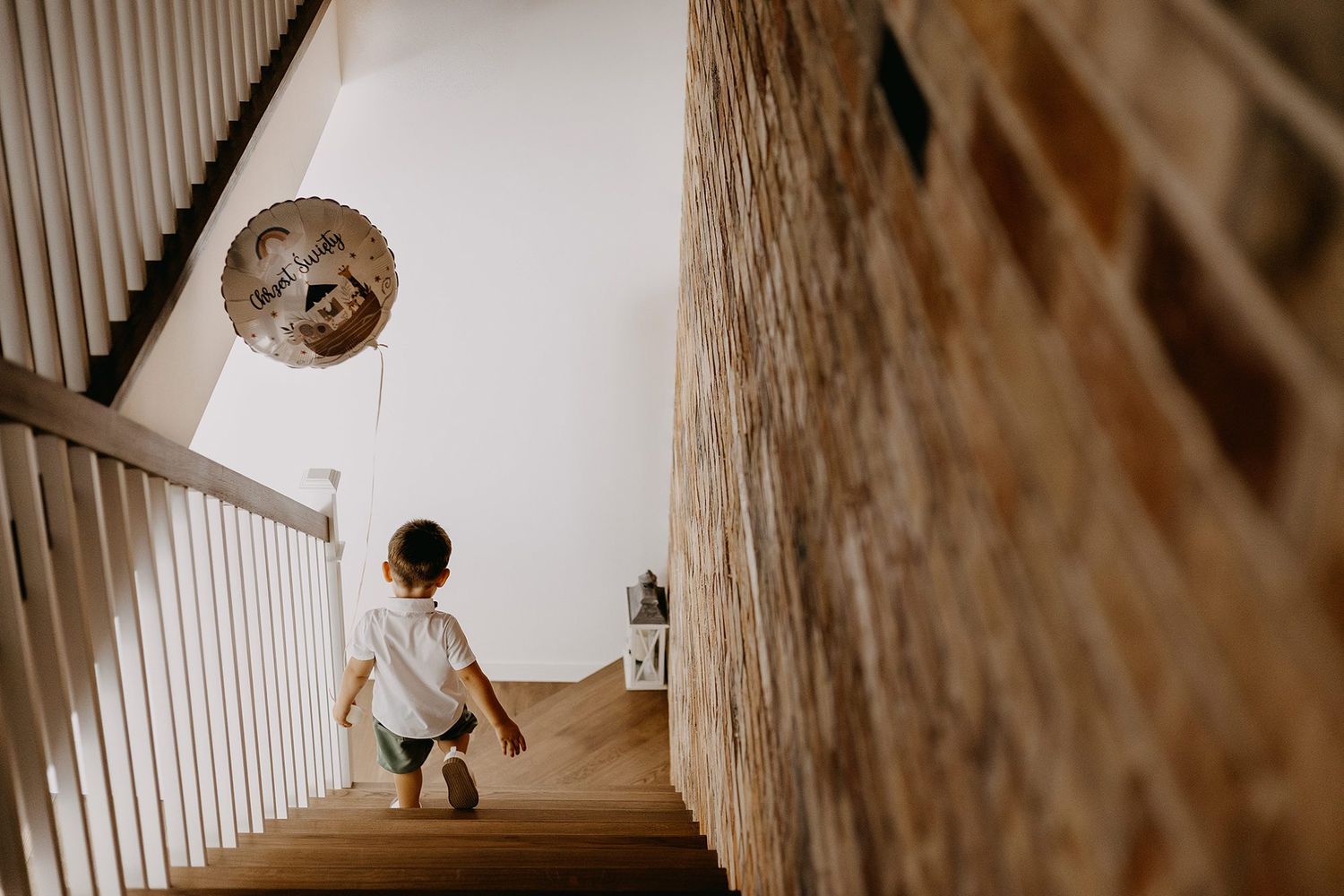 Young child climbing wooden stairs viewed from behind in modern home interior.