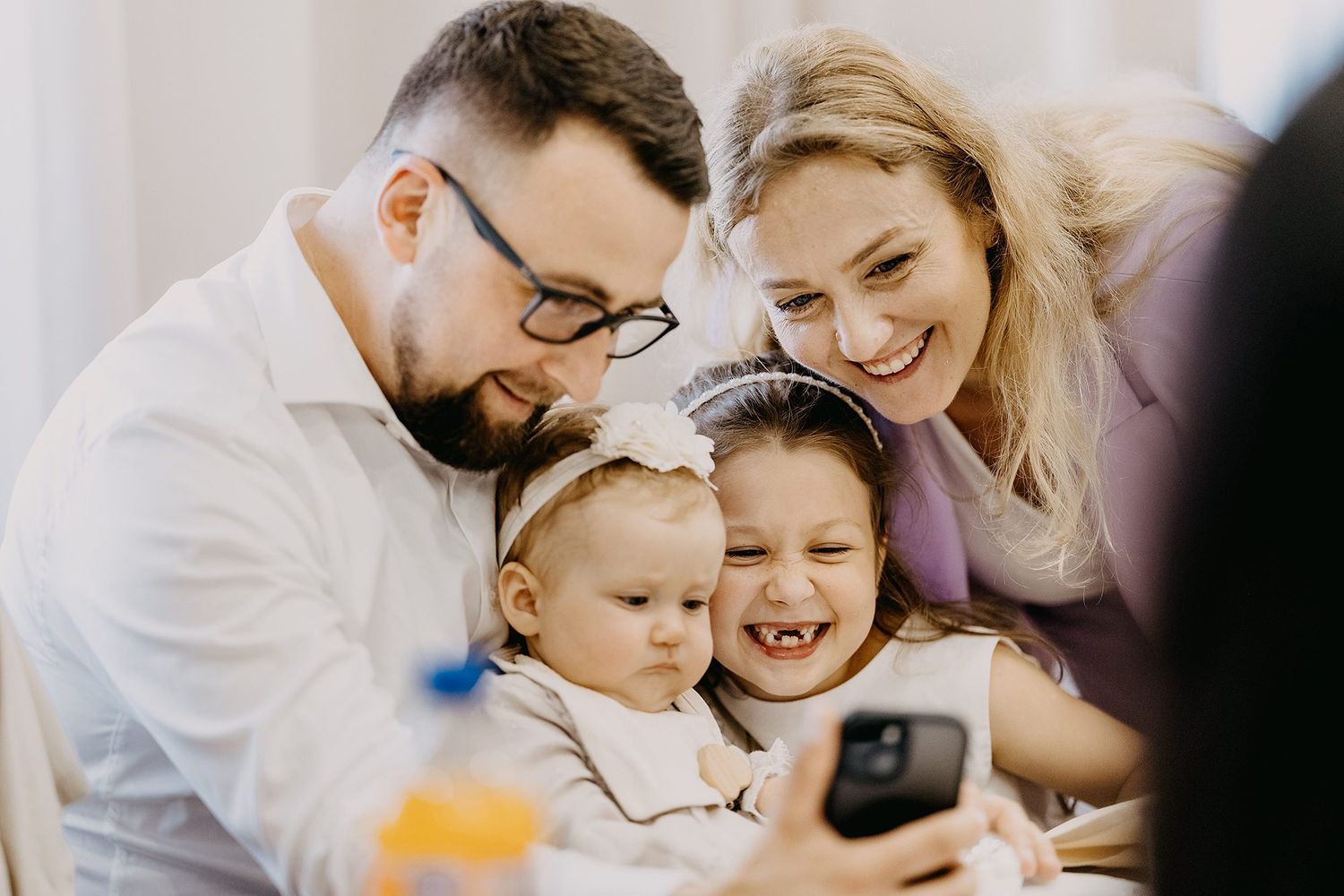 Joyful family with two young children laughing together while looking at a smartphone screen.