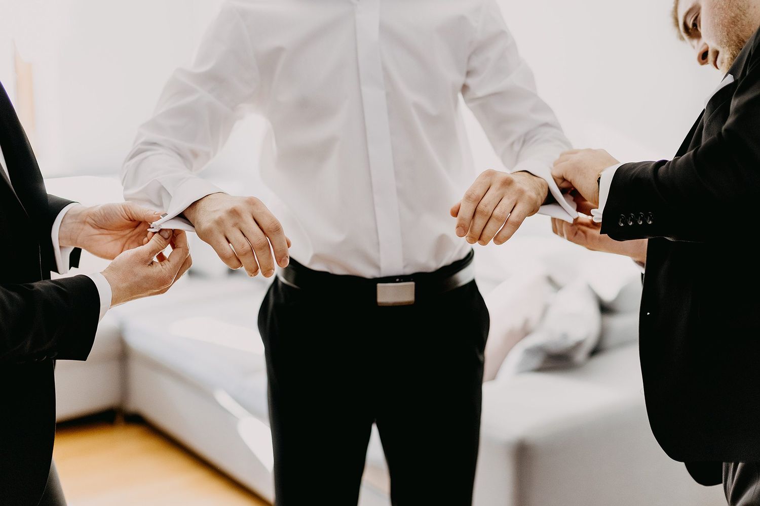 Groomsmen help the groom fasten his cufflinks while preparing for the wedding ceremony.