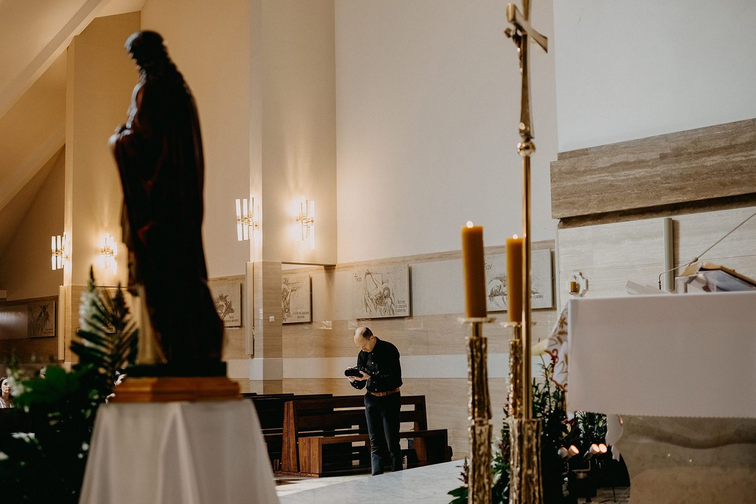 Wedding photographer working near a dark religious statue and altar with candles in a church.