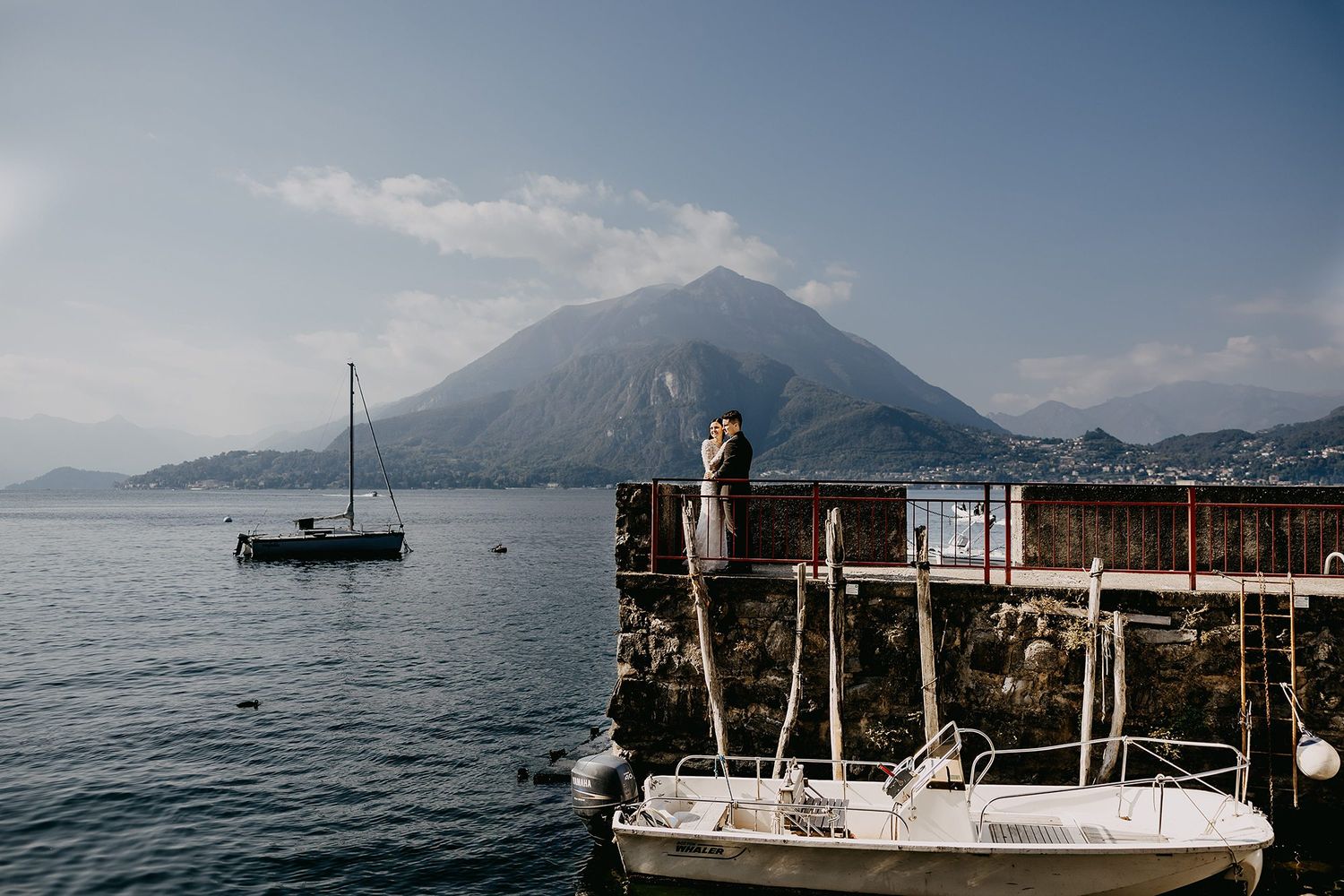 Bride and groom share a romantic moment on a rustic dock overlooking a serene mountain lake.