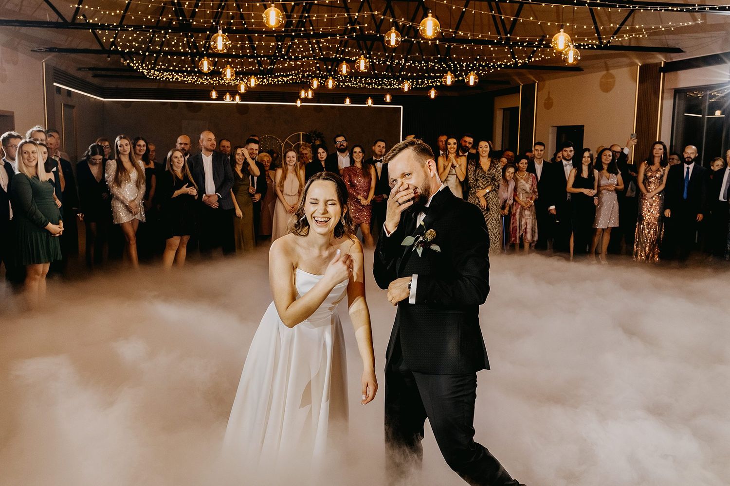 Bride and groom share first dance surrounded by dramatic fog machine clouds at elegant wedding reception.