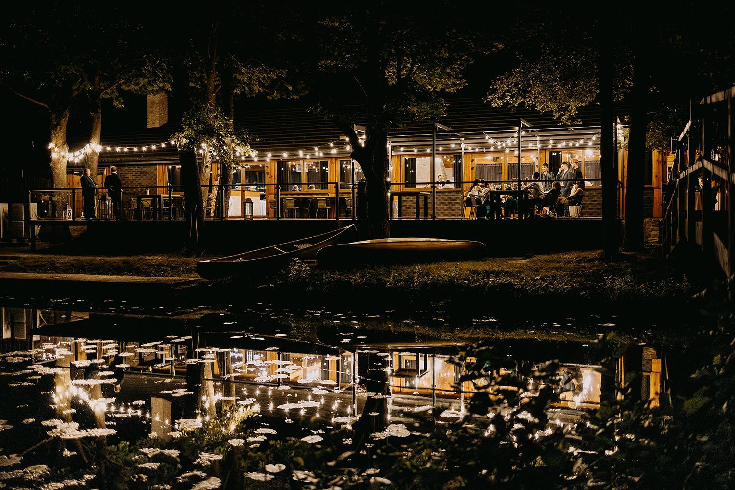 Romantic wedding venue illuminated at night with string lights reflecting beautifully on a pond.