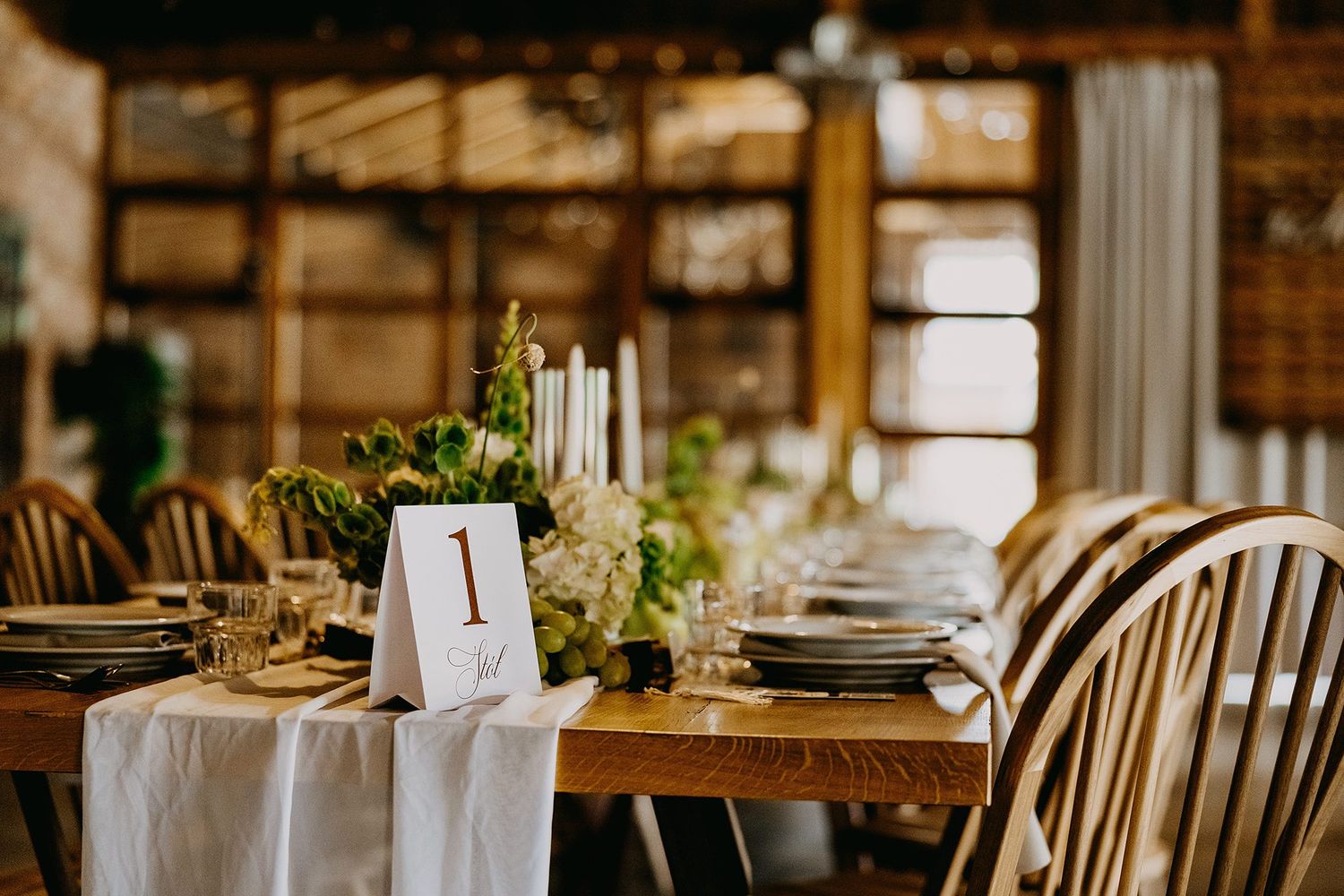 Elegant rustic wedding reception table with white candles, greenery, and numbered place card.