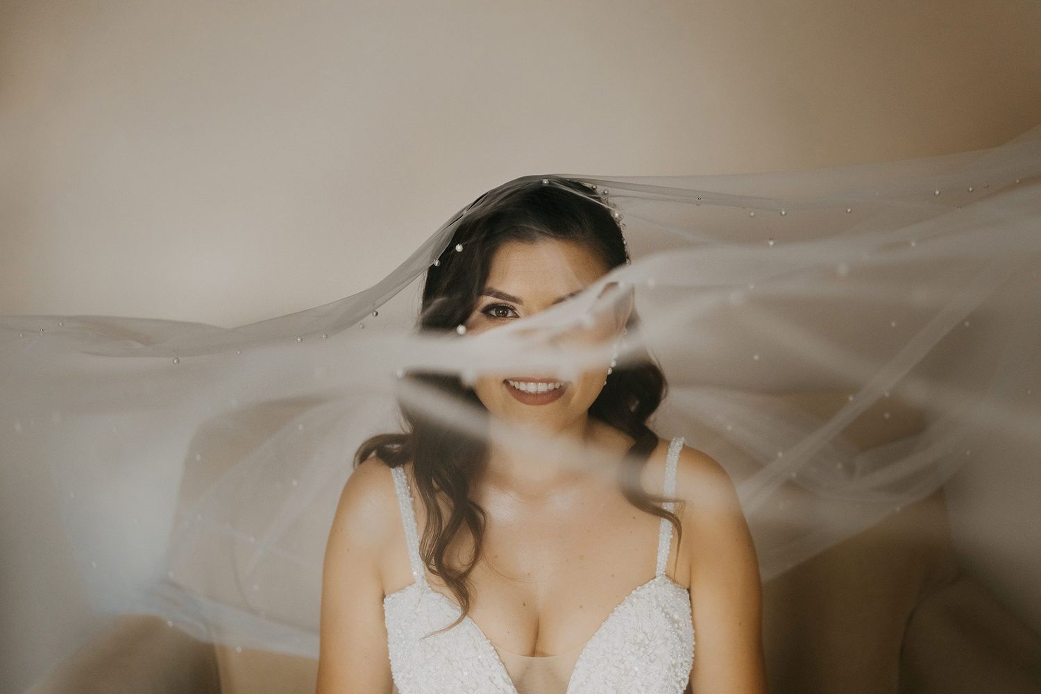 Smiling bride in lace wedding dress with a flowing veil billowing around her face.