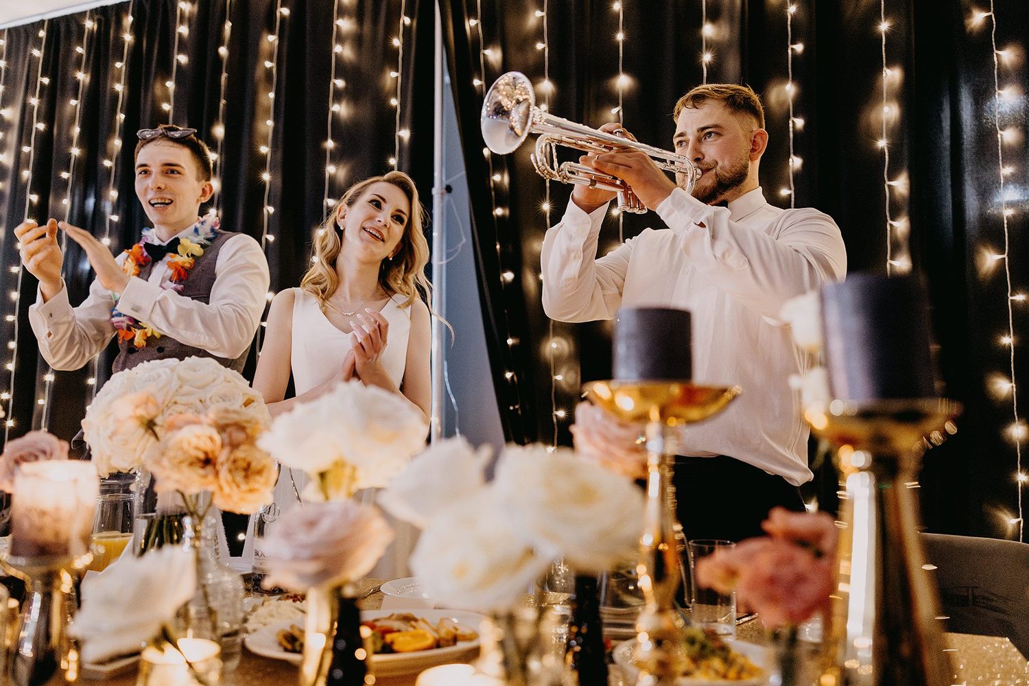 Trumpet musician performing for bride and groom at candlelit wedding reception table.