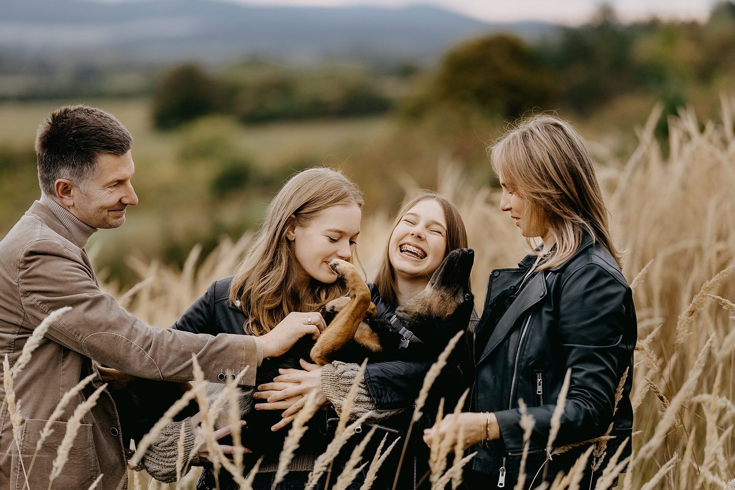 Happy family of four laughing together in an autumn field with tall golden grass.