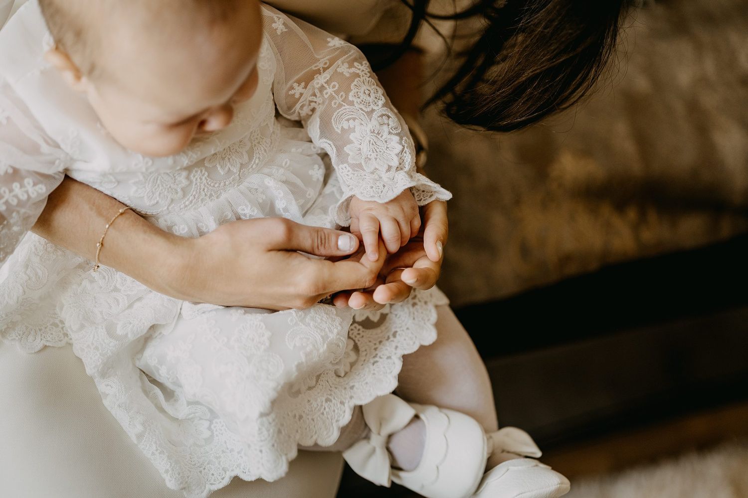 Mother tenderly holds her baby dressed in white lace christening gown during baptism ceremony.