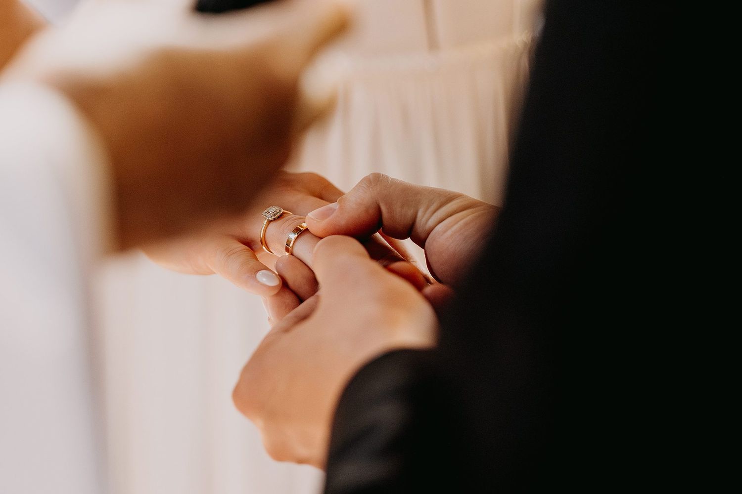 Close-up of a groom placing a gold wedding ring on the bride's finger during a wedding ceremony.
