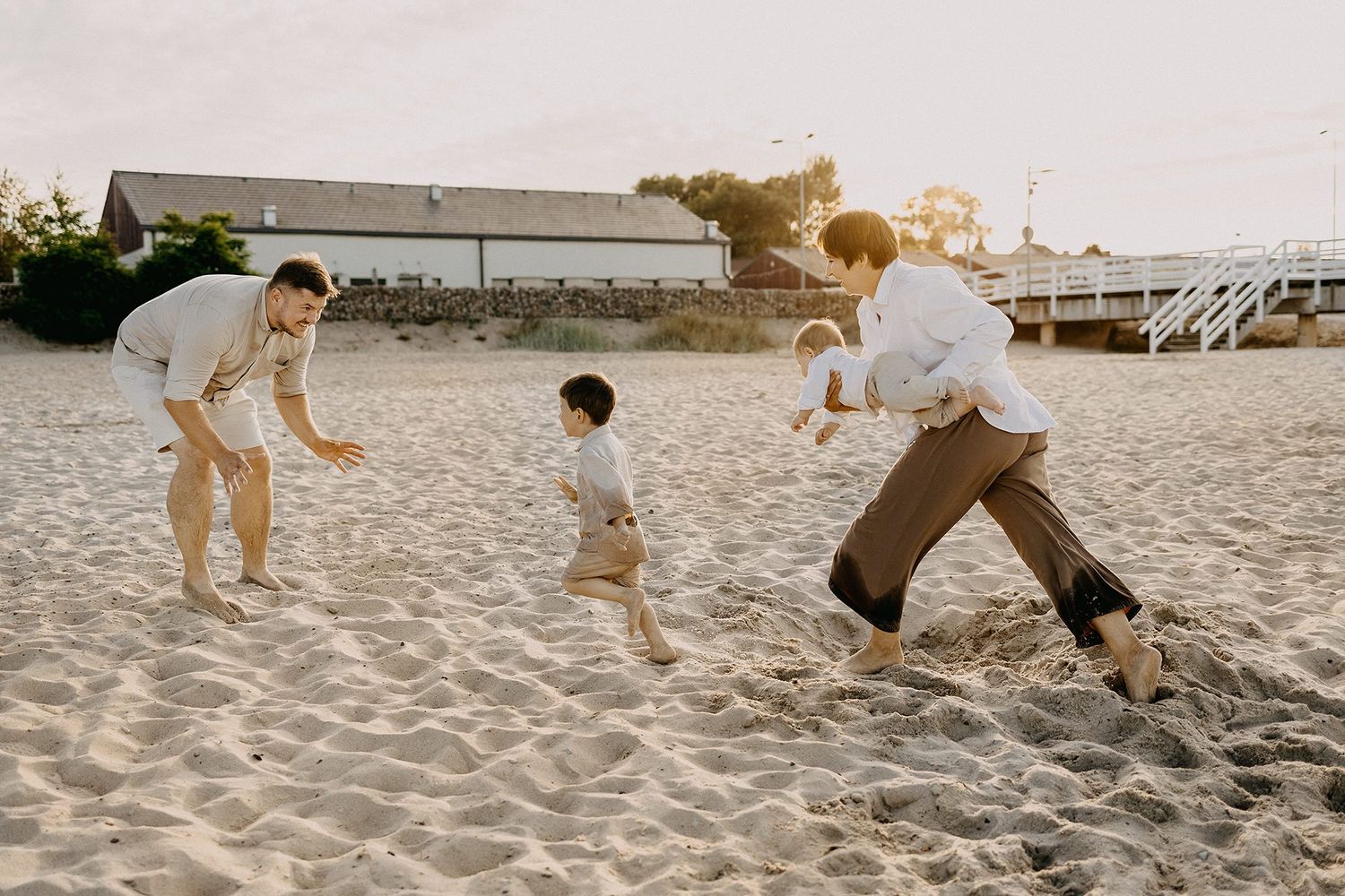 Family of three playing and chasing each other on a sandy beach during warm golden sunset.