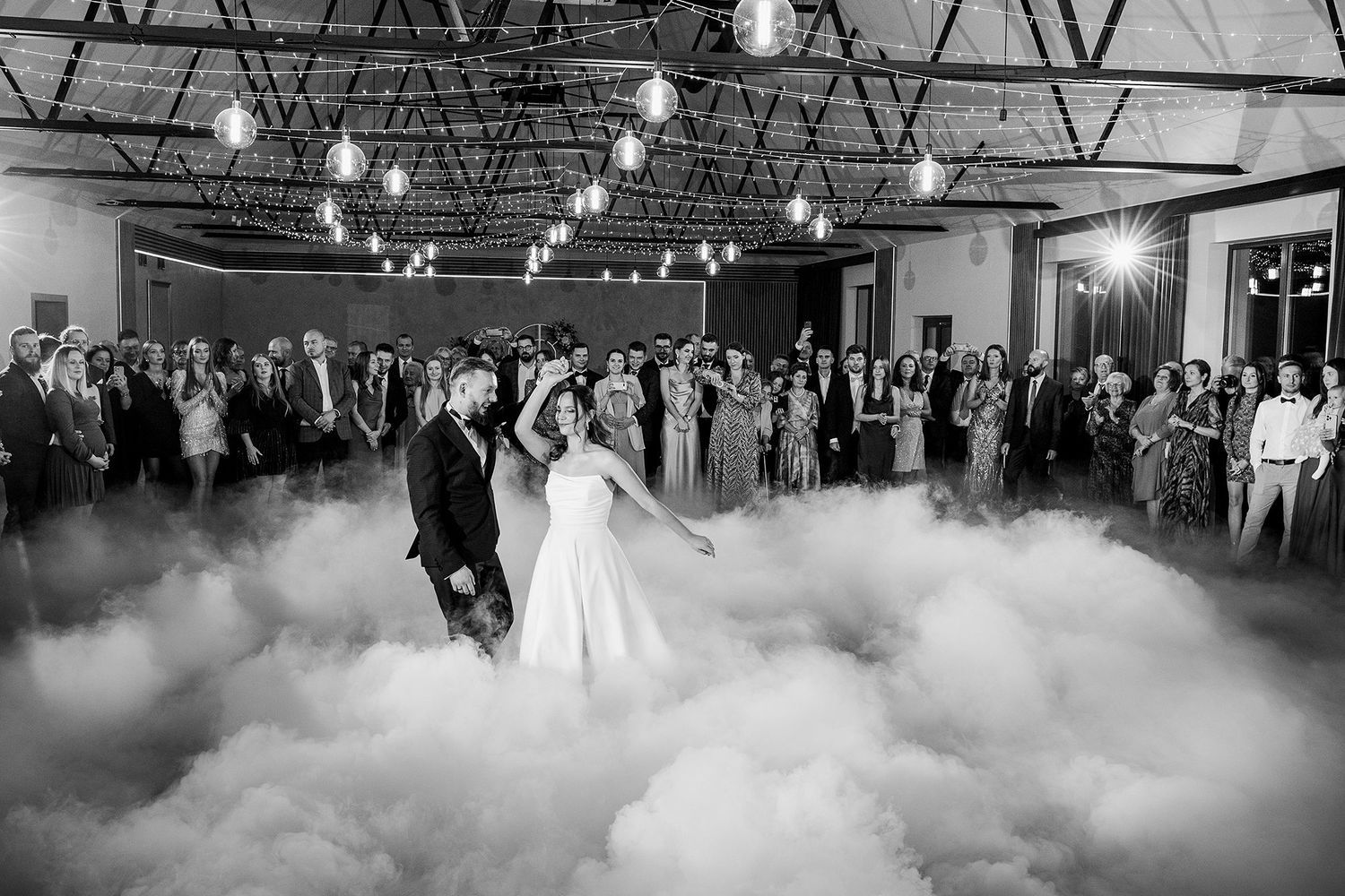 Black and white photo of bride and groom first dance enveloped in dreamy fog at wedding reception.