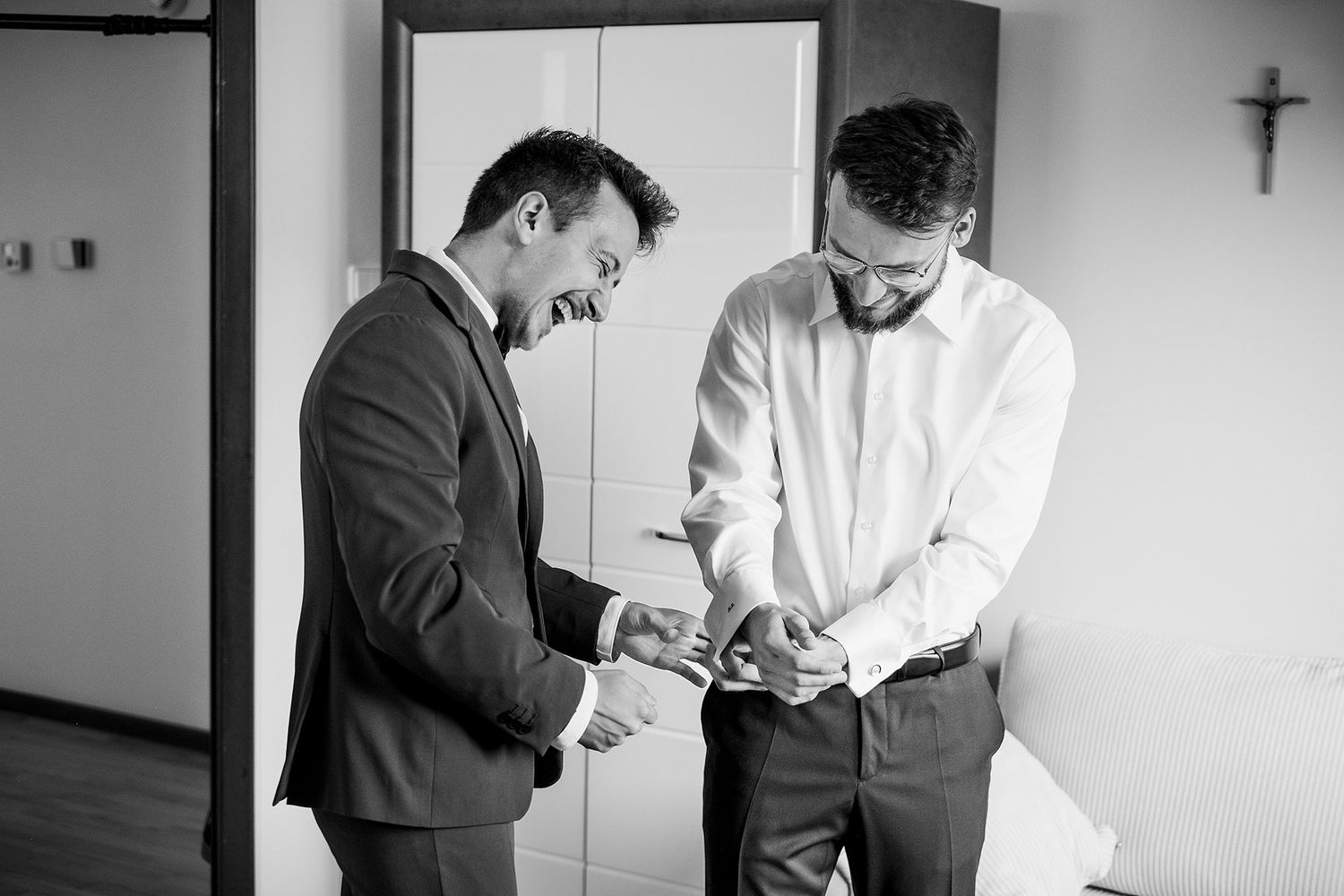Black and white photo of two men helping groom with cufflinks while getting ready for wedding.
