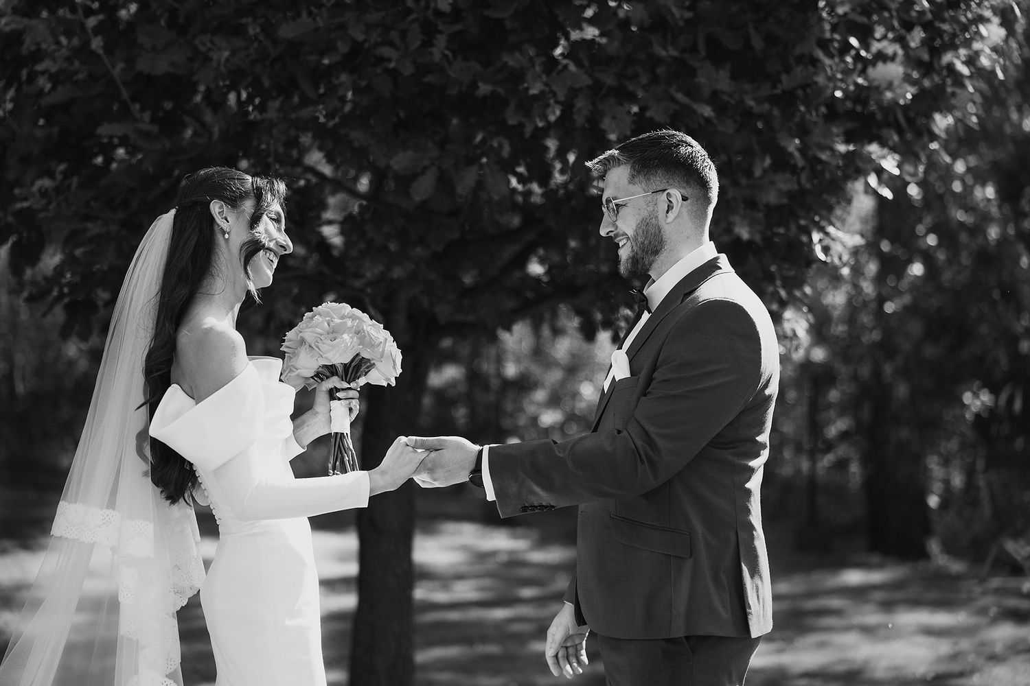 Black and white photo of a bride and groom sharing a tender moment outdoors during their wedding ceremony.