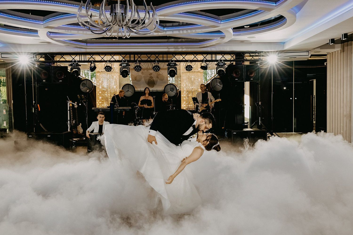 Bride and groom sharing first dance surrounded by dramatic fog on a grand ballroom stage.