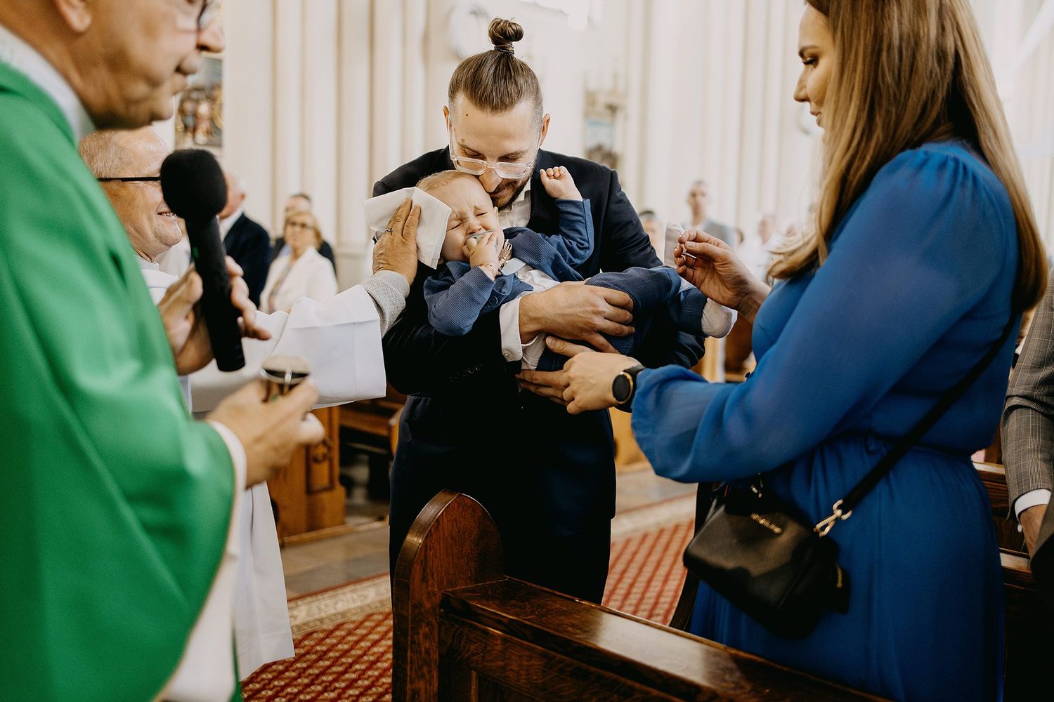 Godfather presents baby to priest during Catholic baptism ceremony at church altar.