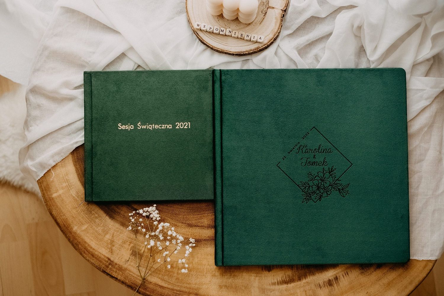 Two green velvet photo albums with gold and dark embossed text on rustic wooden surface.
