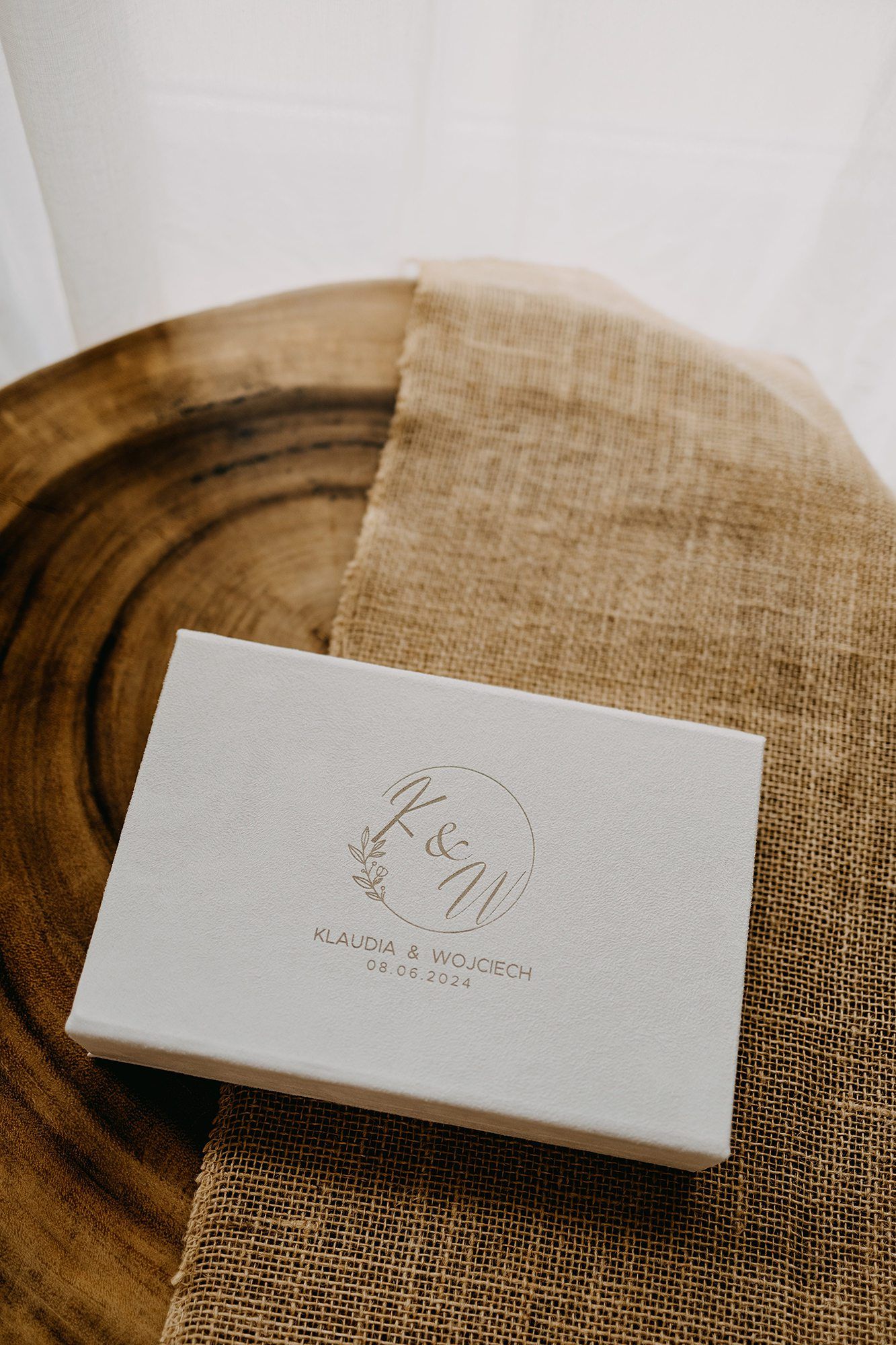 Elegant gray linen wedding box with gold monogram K&W for Klaudia & Wojciech on wooden surface.