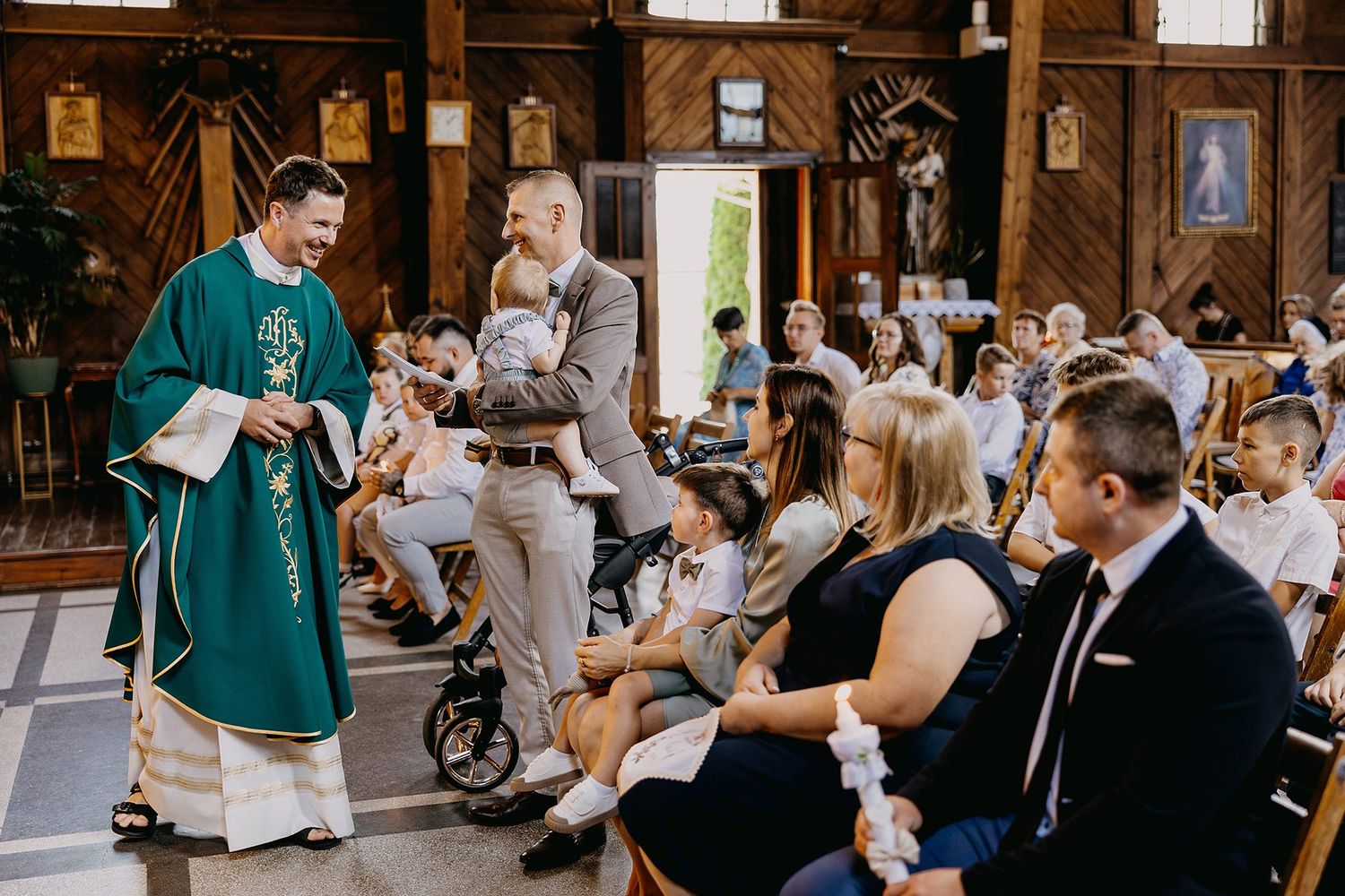 Catholic priest in green vestments greeting family holding baby during baptism Mass ceremony.