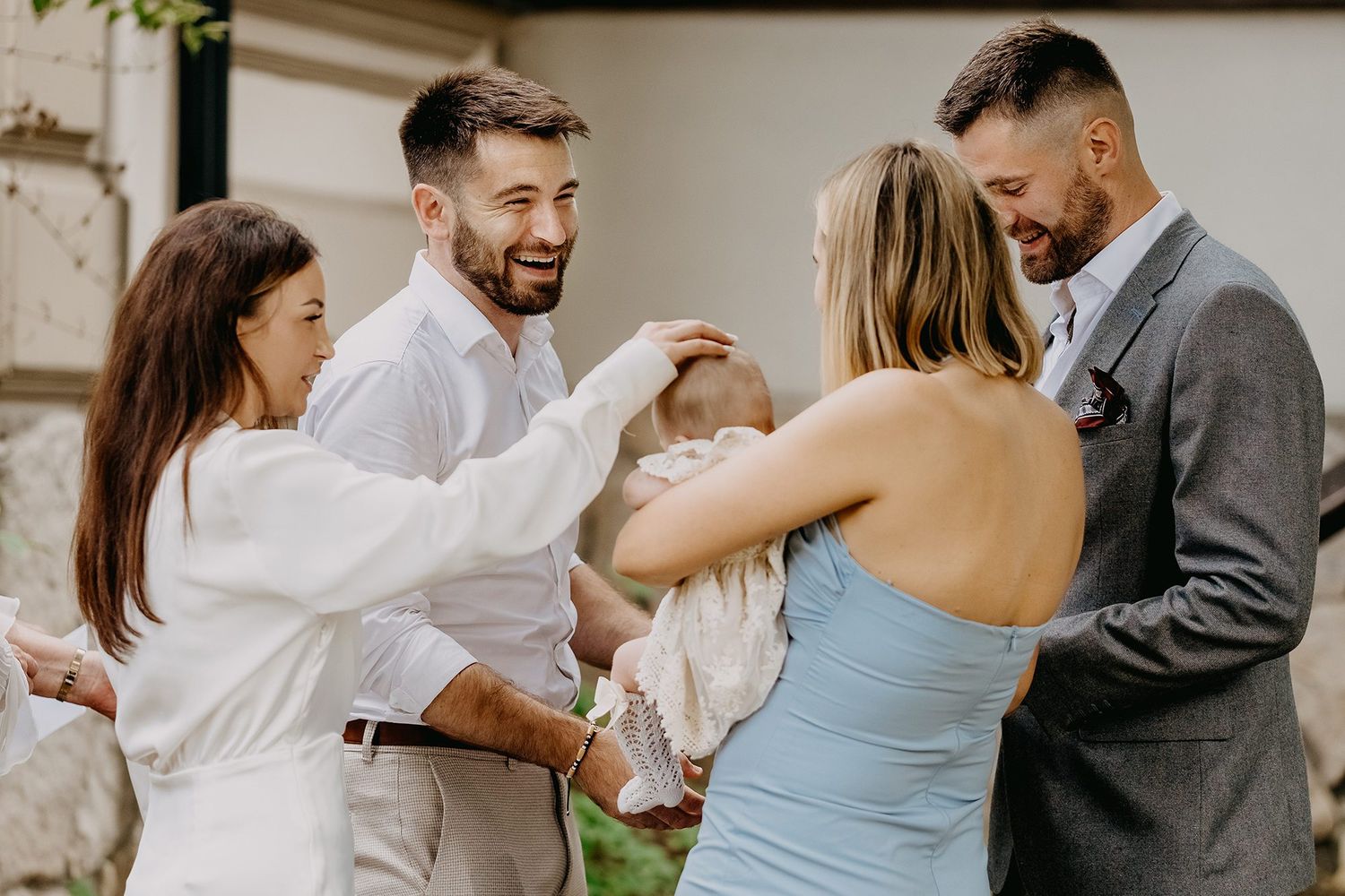 Happy group of adults admiring and celebrating a newborn baby outdoors at a christening gathering.