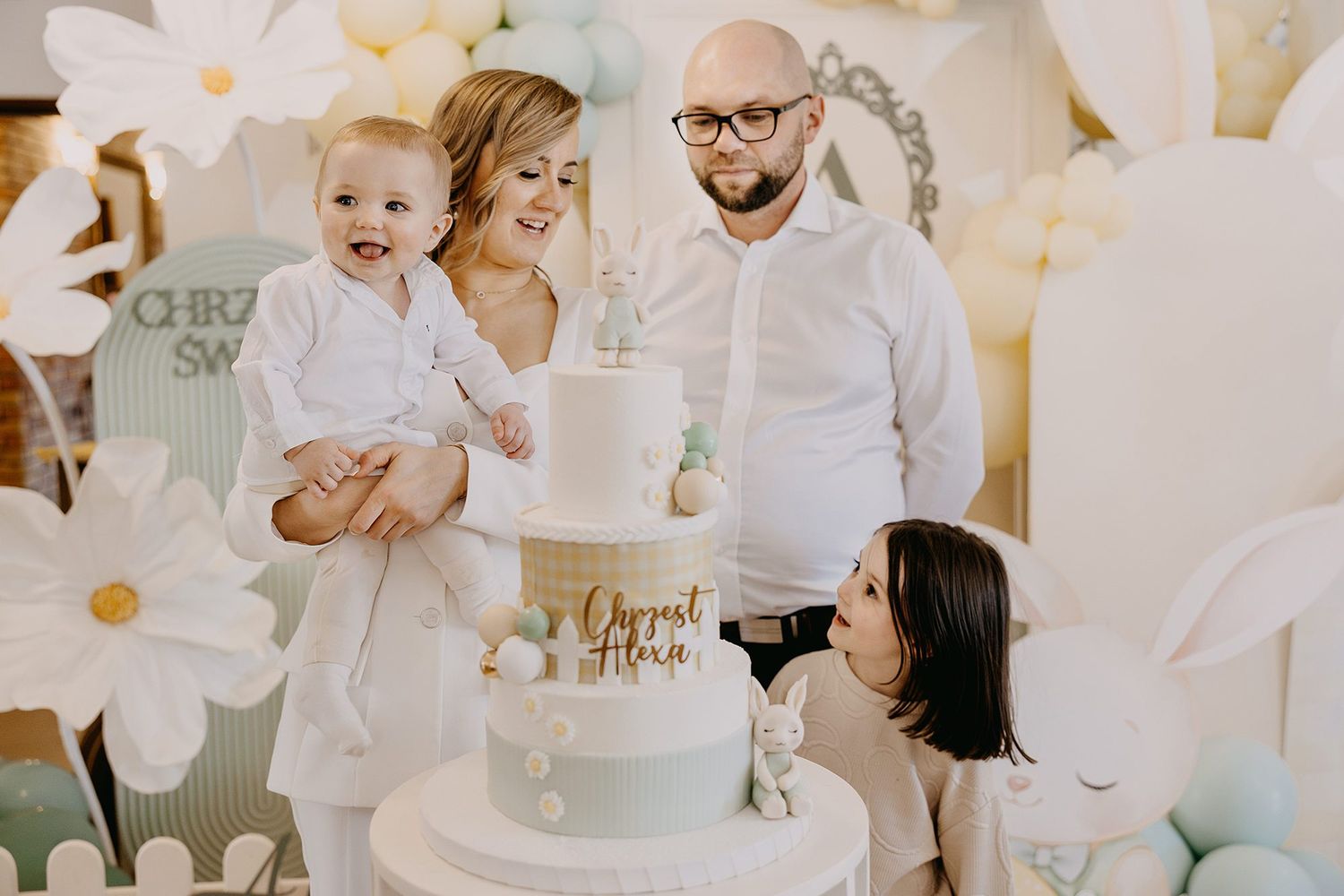 A family poses with a elegant christening cake decorated with bunny figurines.