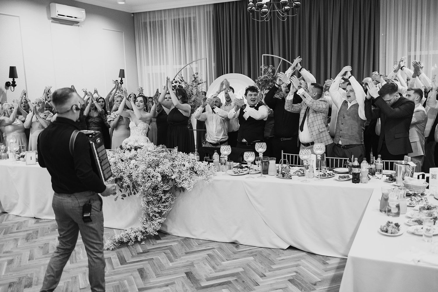 Wedding guests raise hands during lively reception celebration in black and white photo.