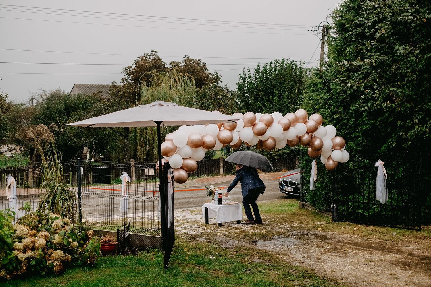 Person with umbrella walking under a balloon arch decoration on a rainy wedding day.
