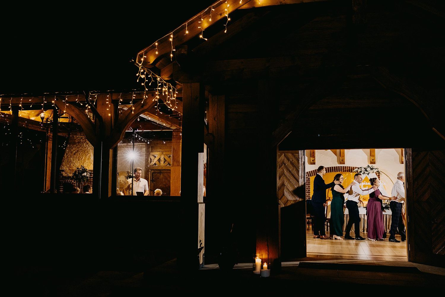 Nighttime exterior view of rustic barn wedding venue glowing warmly with guests celebrating inside.