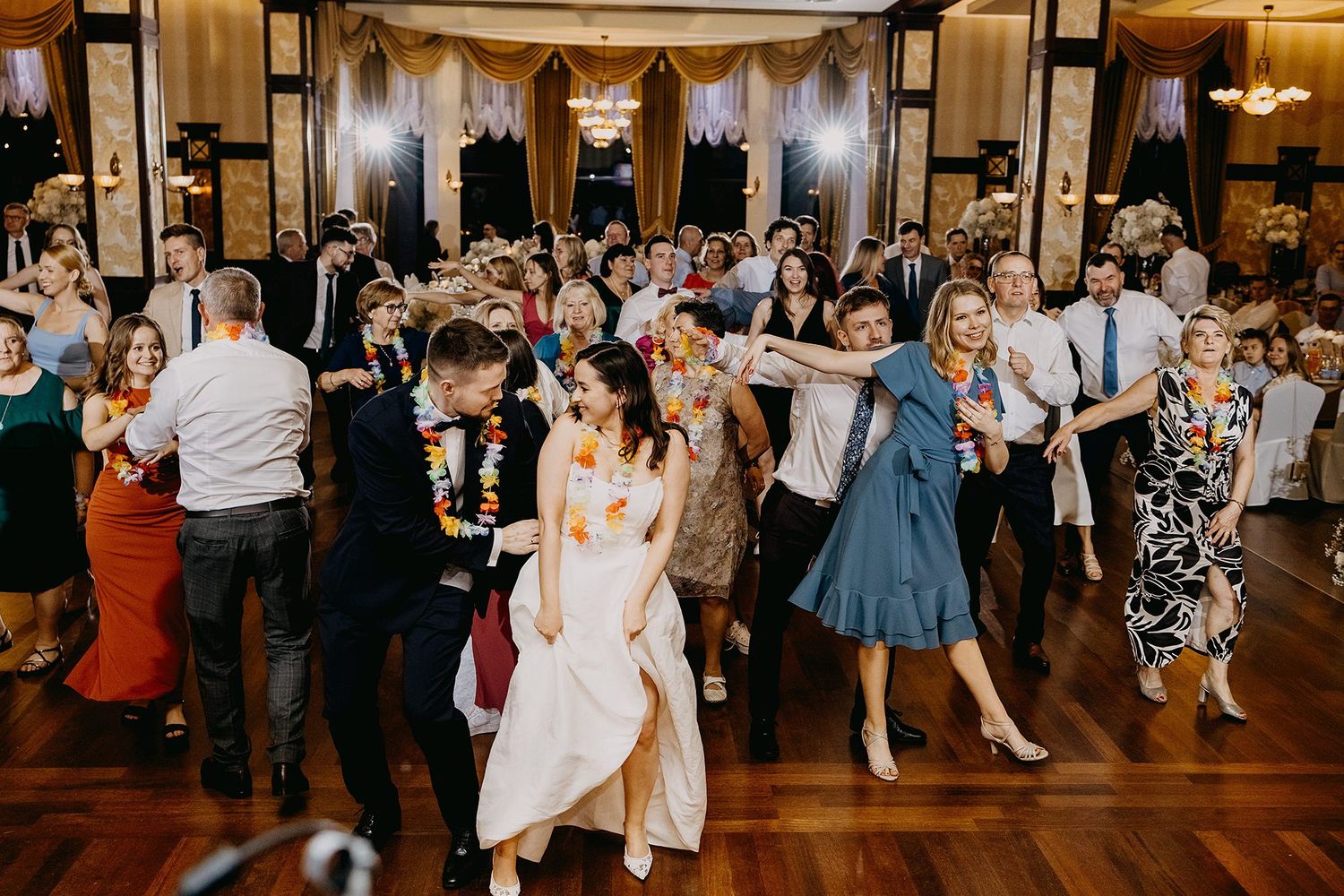 Bride and wedding guests dancing joyfully on the dance floor at a ballroom reception.