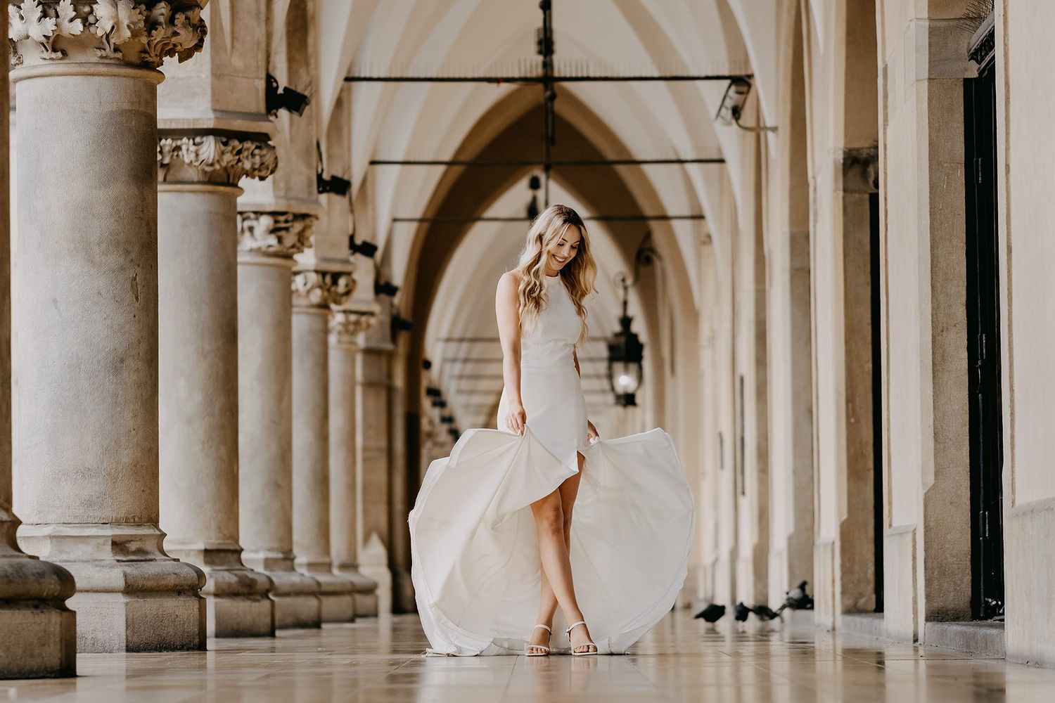 Bride in flowing white gown twirling under Gothic arches of historic building.