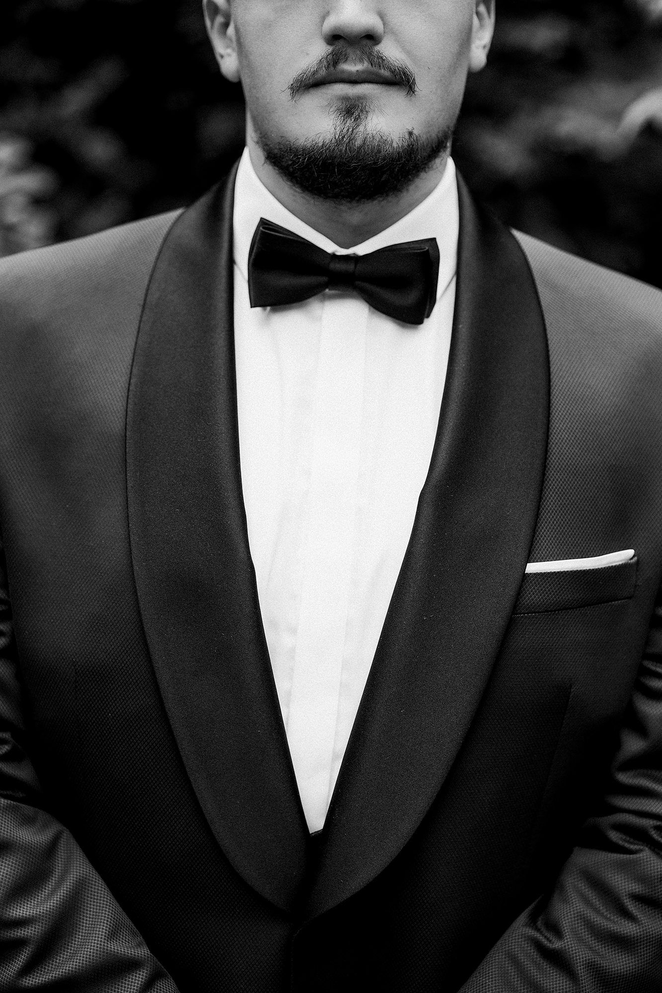 Groom in black tuxedo with bow tie and pocket square, black and white photo.