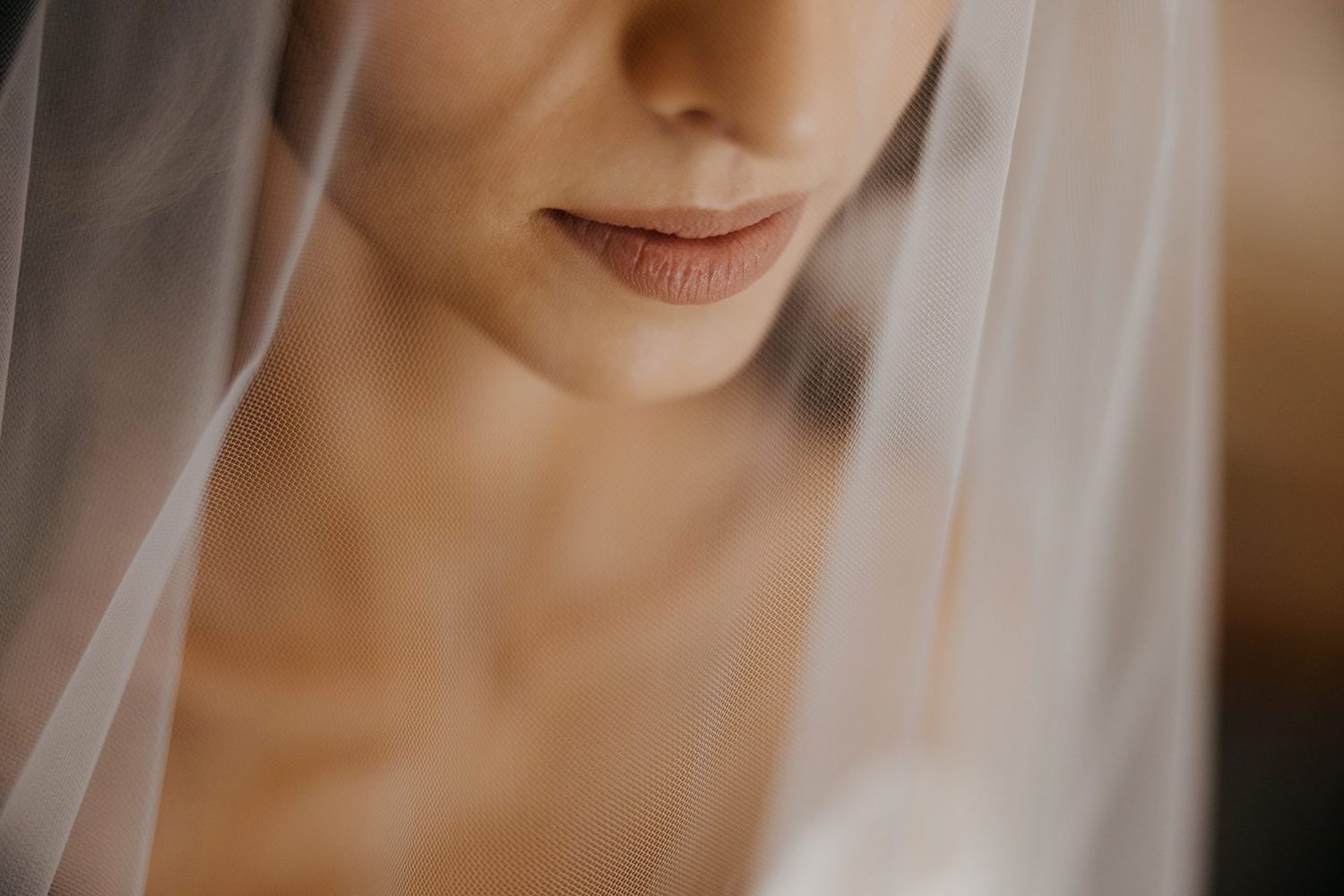 Close-up of a bride's lips and décolletage partially covered by a delicate white wedding veil.